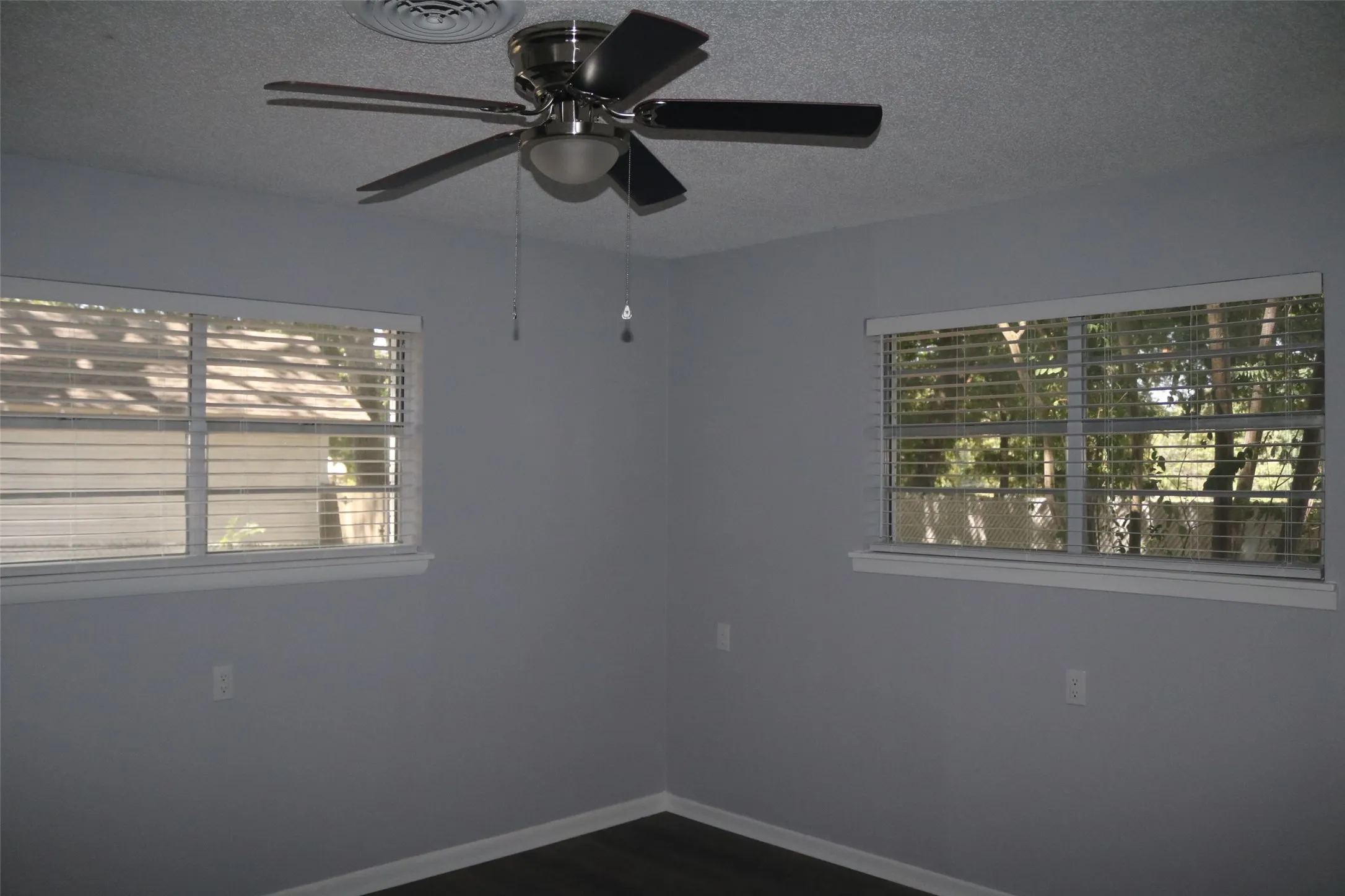 Dual windows with white blinds, neutral wall paint, ceiling fan with brushed nickel finish, and dark wood-finish flooring