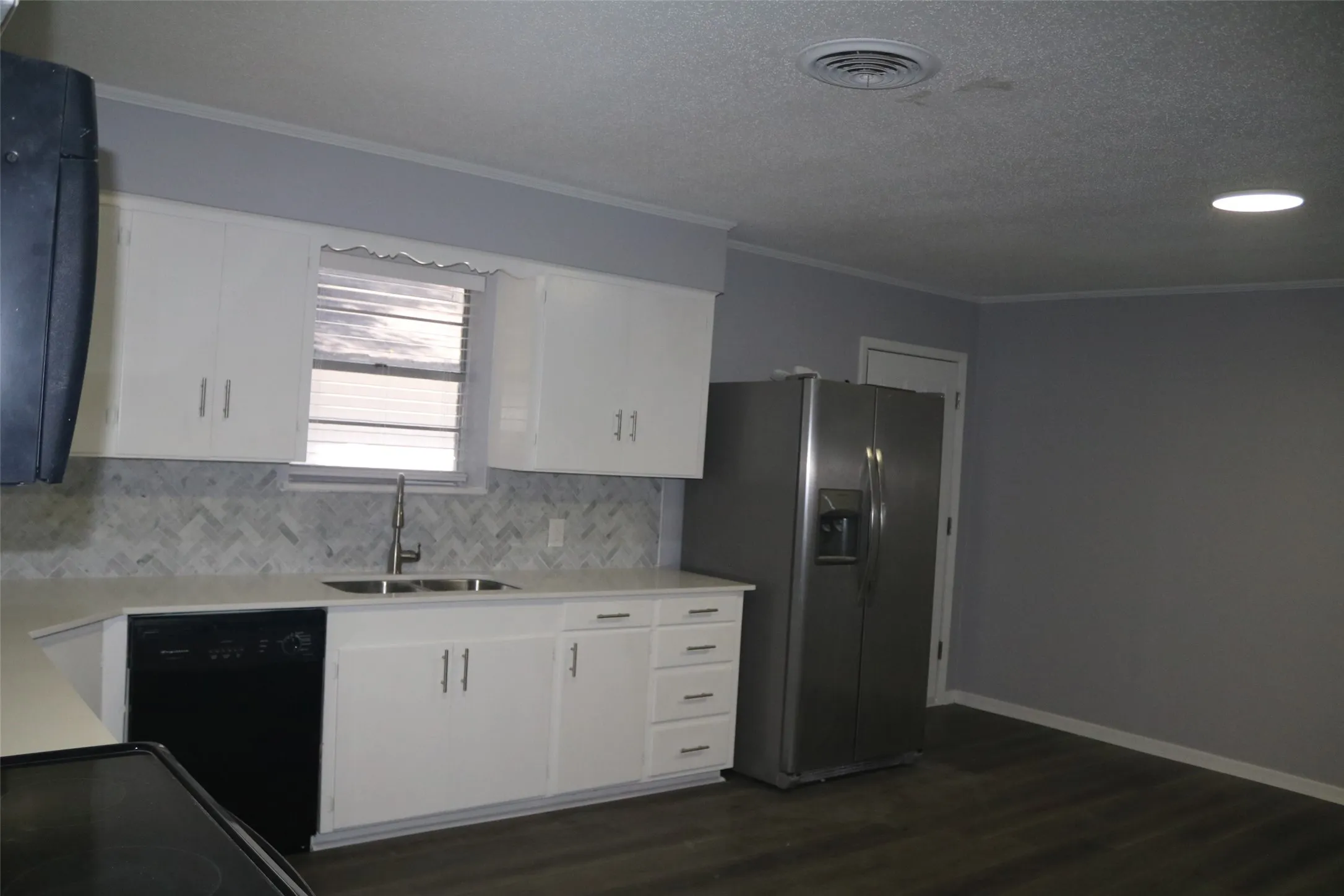 Kitchen featuring white cabinetry, light countertops, herringbone pattern backsplash, and wood-finish flooring