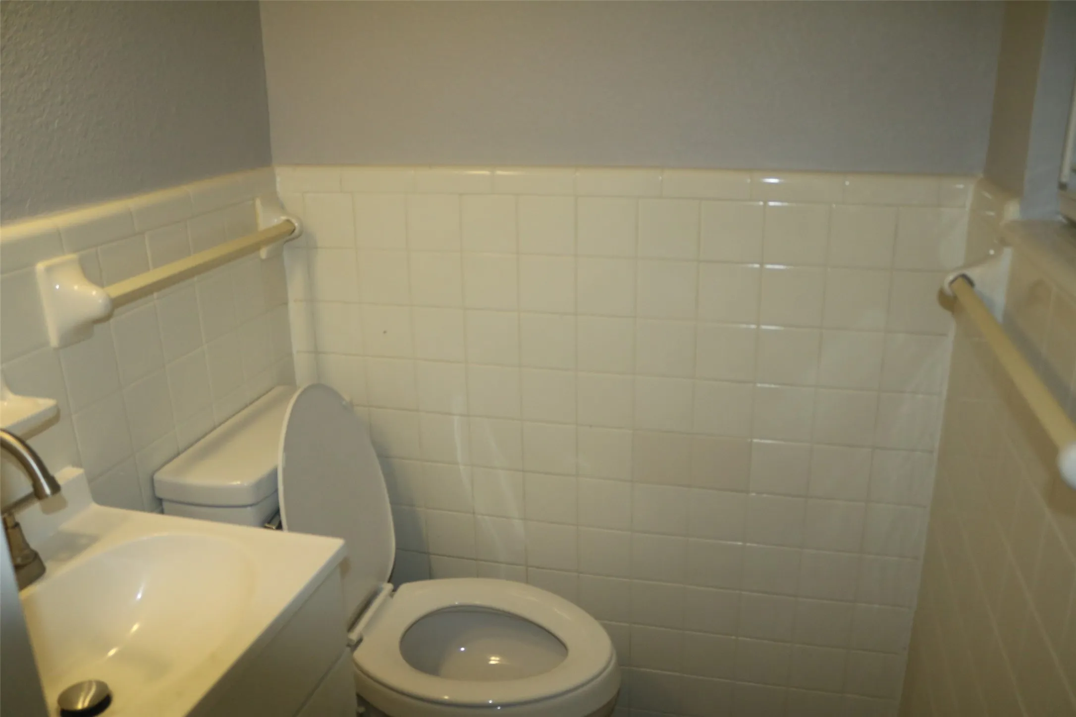 White square-tiled walls with a coordinating trim, complete with a toilet and a white vanity featuring an integrated sink and a brushed metal faucet