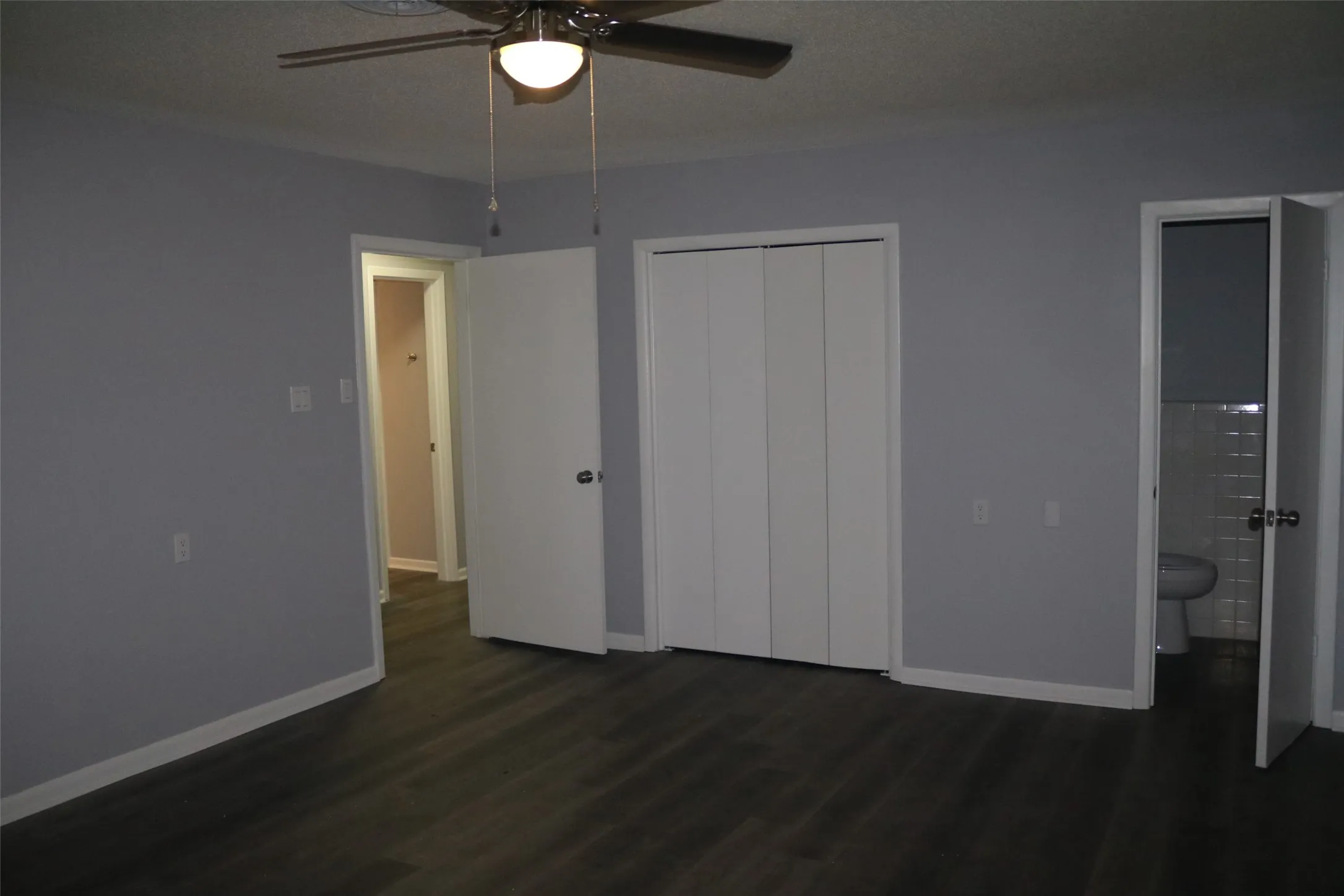 Wood-finish flooring, ceiling fan with integrated lighting, bi-fold closet doors, and light gray wall paint