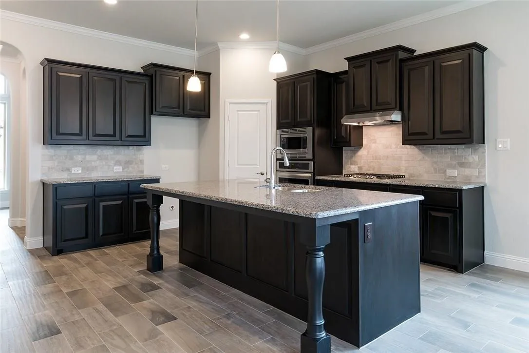 Kitchen featuring dark cabinetry, speckled countertops, stainless steel appliances, a center island with a sink, and wood-finish flooring