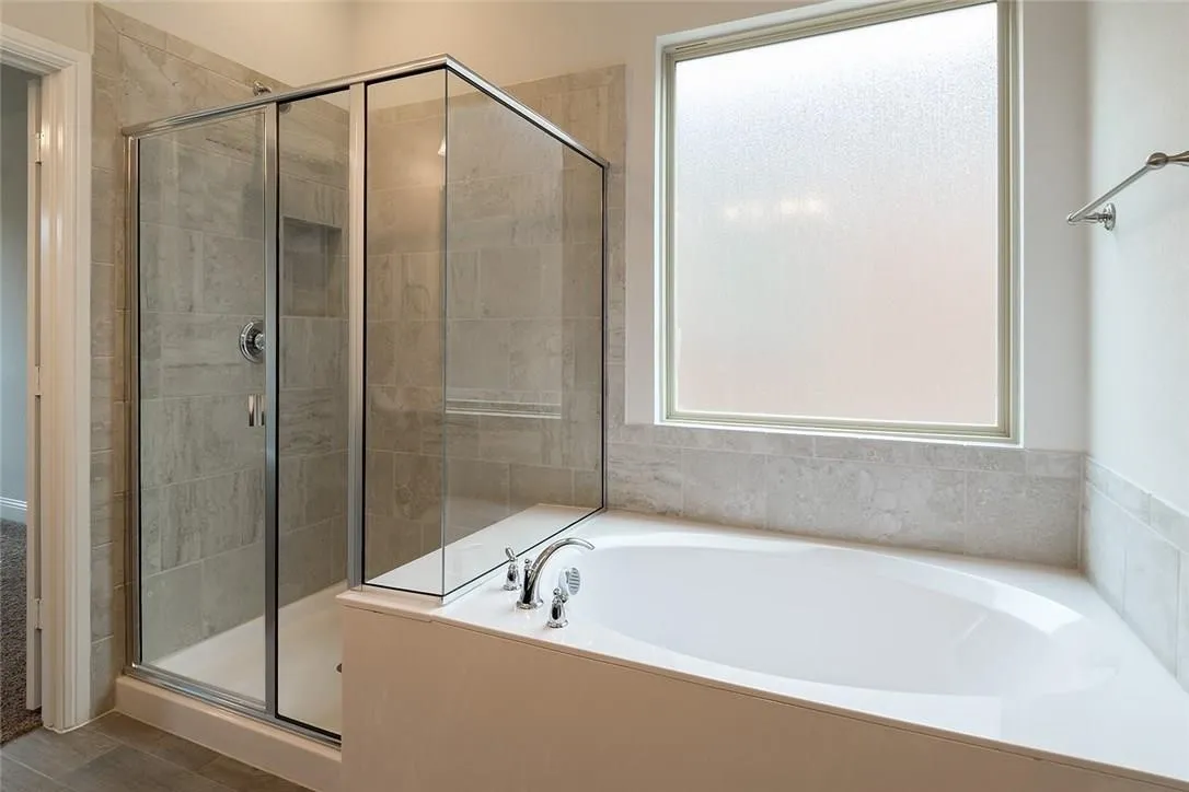Soaking tub with deck-mounted fixtures, enclosed glass shower with tiled walls, and a frosted window
