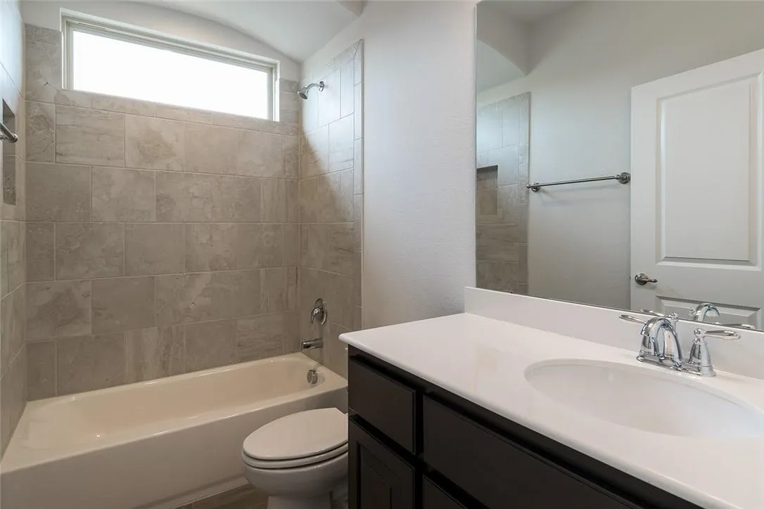 Full-height tile bath surround, built-in shower niche, chrome fixtures, white vanity countertop, dark wood-finish cabinetry