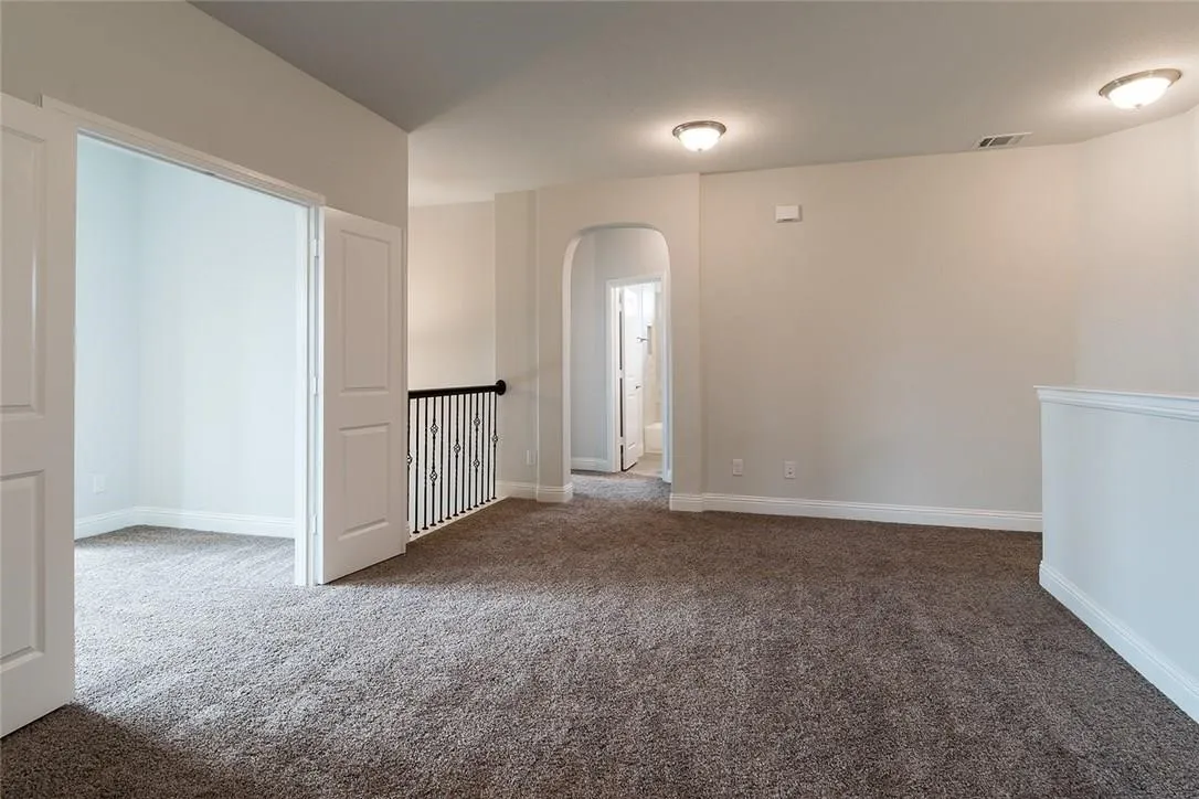 Carpeted room with neutral wall tones, arched doorway, recessed lighting, and a wrought iron railing