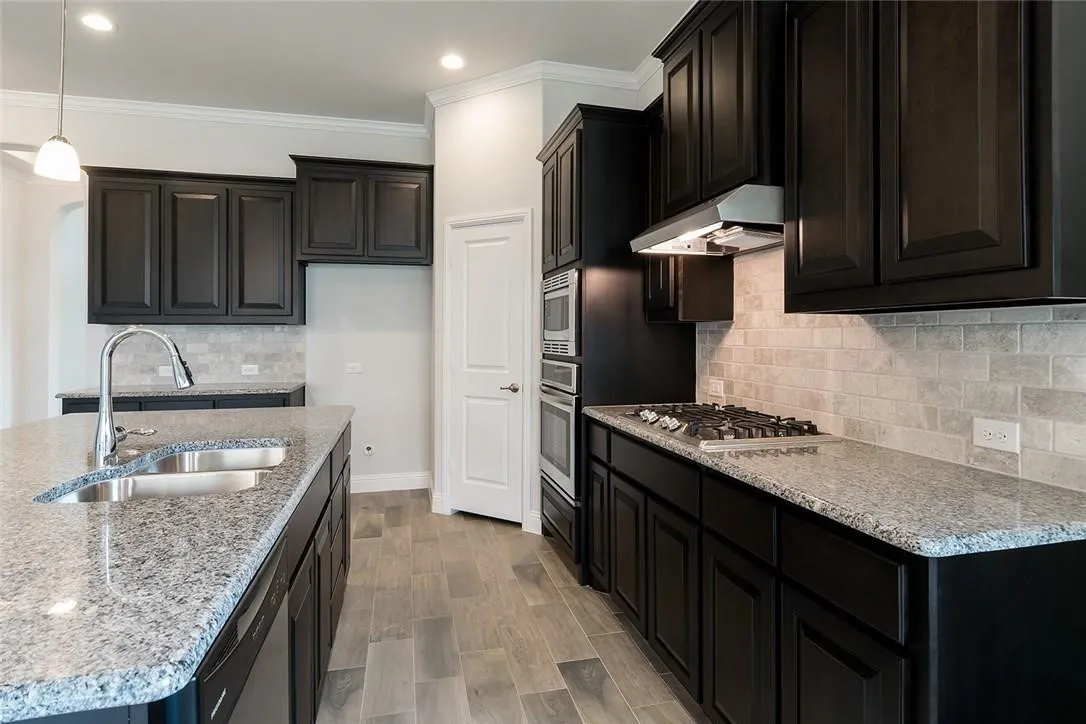 Kitchen featuring dark wood-finish cabinetry, granite countertops, tile backsplash, stainless steel appliances, and wood-look flooring