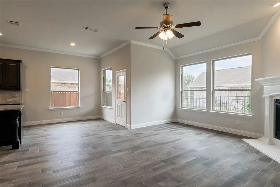 Vaulted ceiling with a ceiling fan, crown molding, wood-finish flooring, multiple windows, and a built-in fireplace
