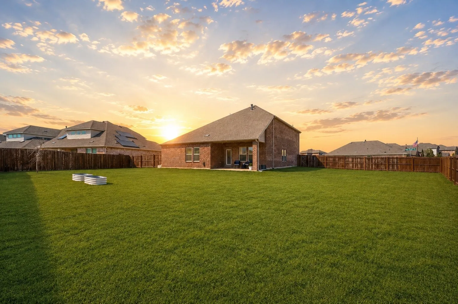 Expansive green lawn, brick exterior with covered patio, and wood privacy fencing