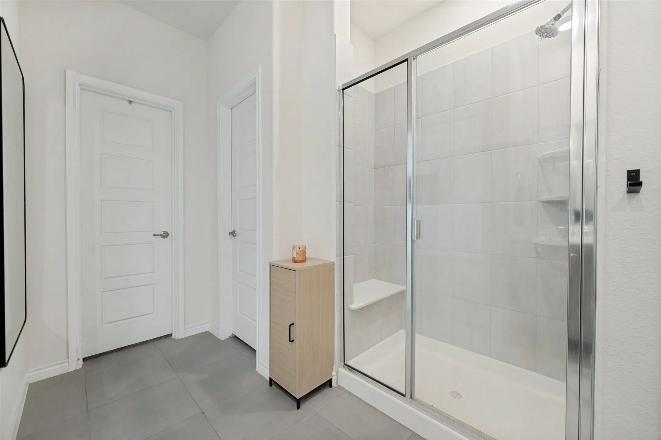 Glass-enclosed shower with a built-in bench and recessed shelving, accompanied by large format floor tiles