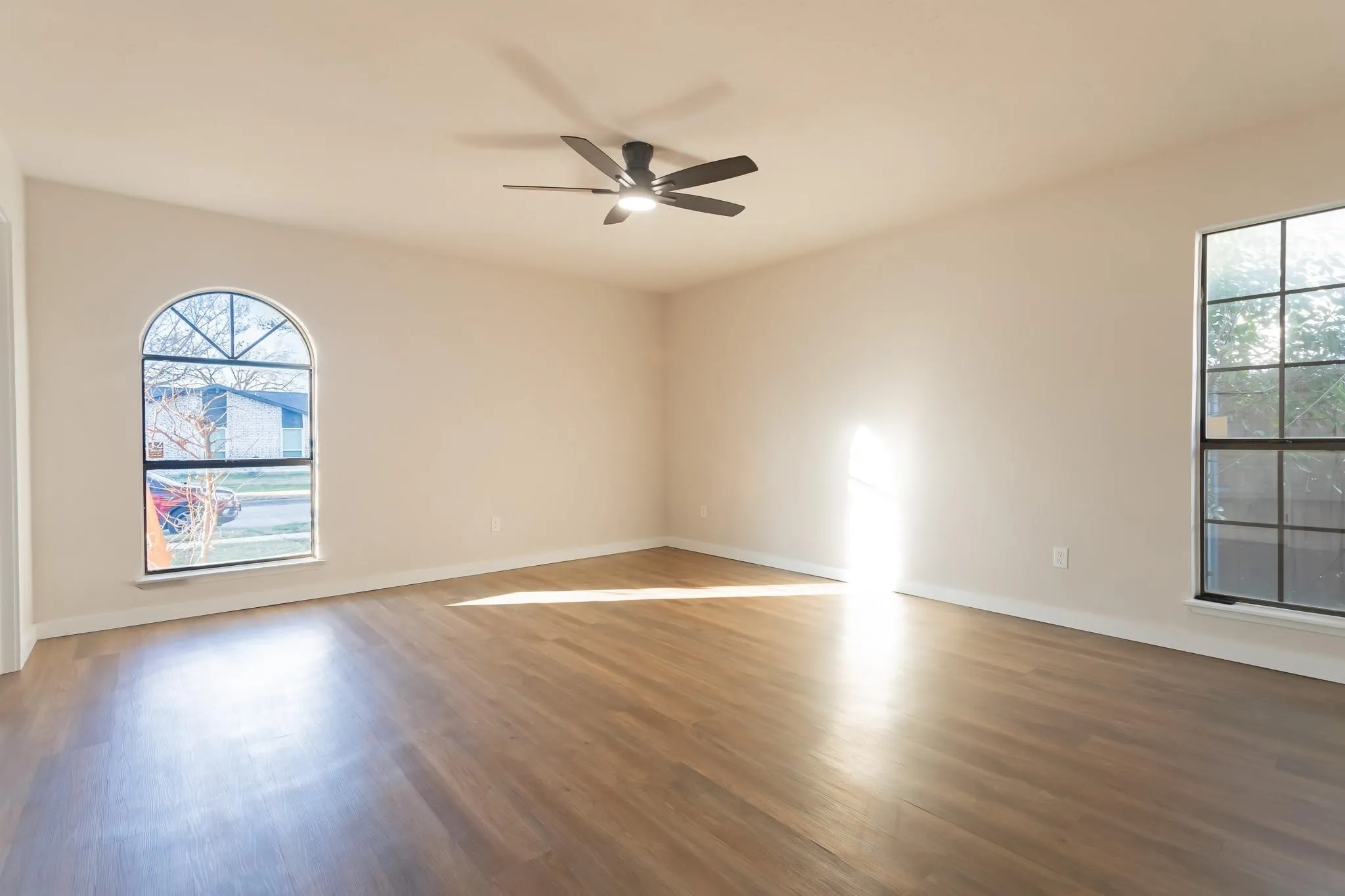 Expansive room featuring wood-finish flooring, a contemporary ceiling fan, and multiple windows including an arched window