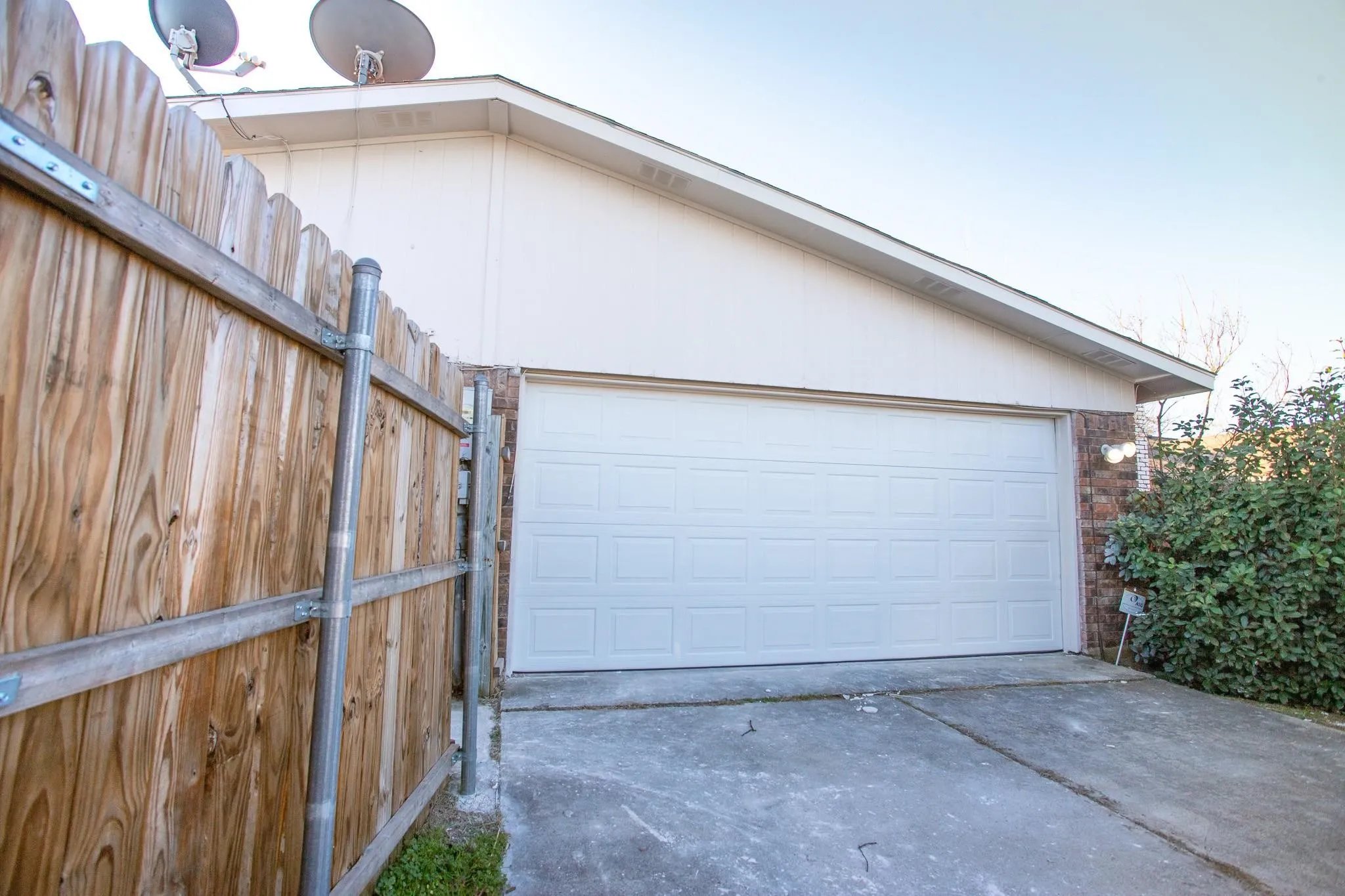 Attached two-car garage with a panel door, concrete driveway, wood privacy fence, and exterior lighting