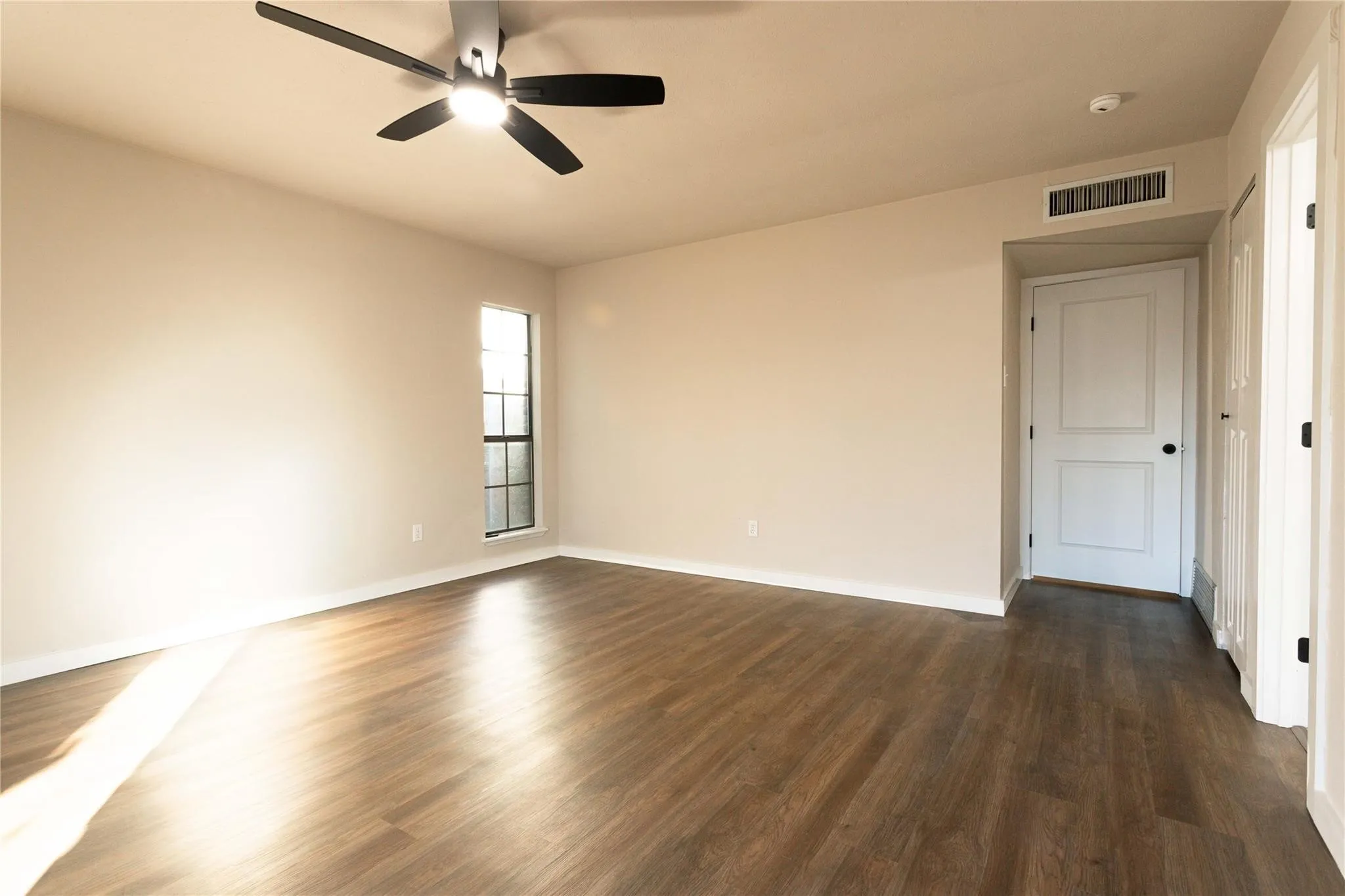 Wood-finish flooring, ceiling fan with integrated lighting, white paneled doors, and a window with horizontal muntins