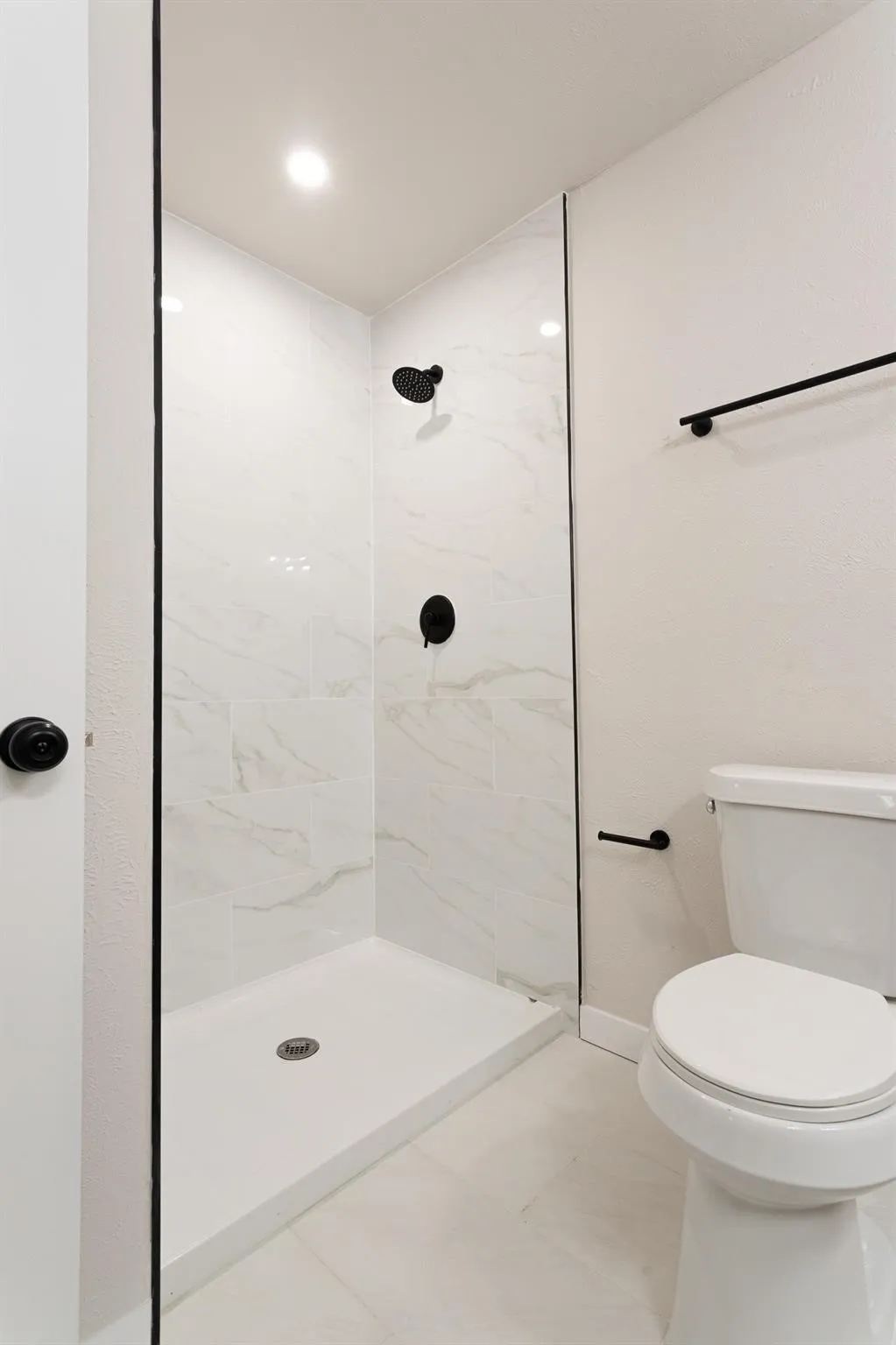 Walk-in shower with clear glass enclosure, white-veined tile surround, matte black fixtures, and recessed lighting