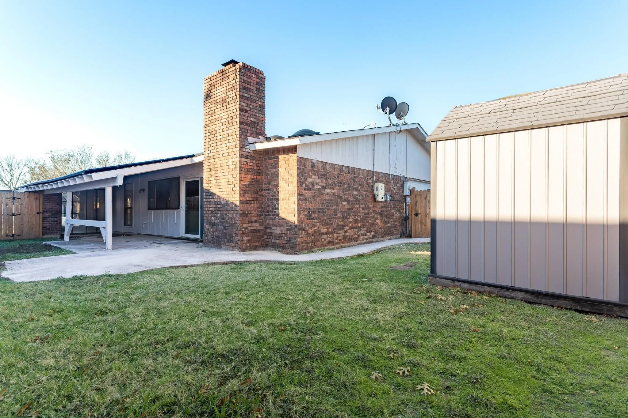 Expansive lawn with a detached storage shed, brick exterior, covered patio, and a privacy fence