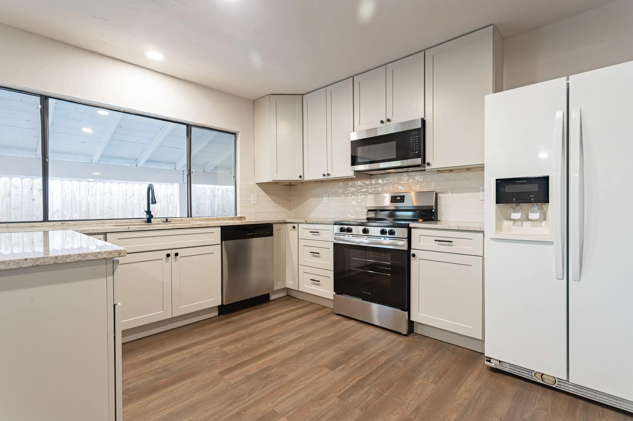Spacious kitchen featuring white cabinetry, light-toned countertops, wood-finish flooring, stainless steel appliances, and a tile backsplash
