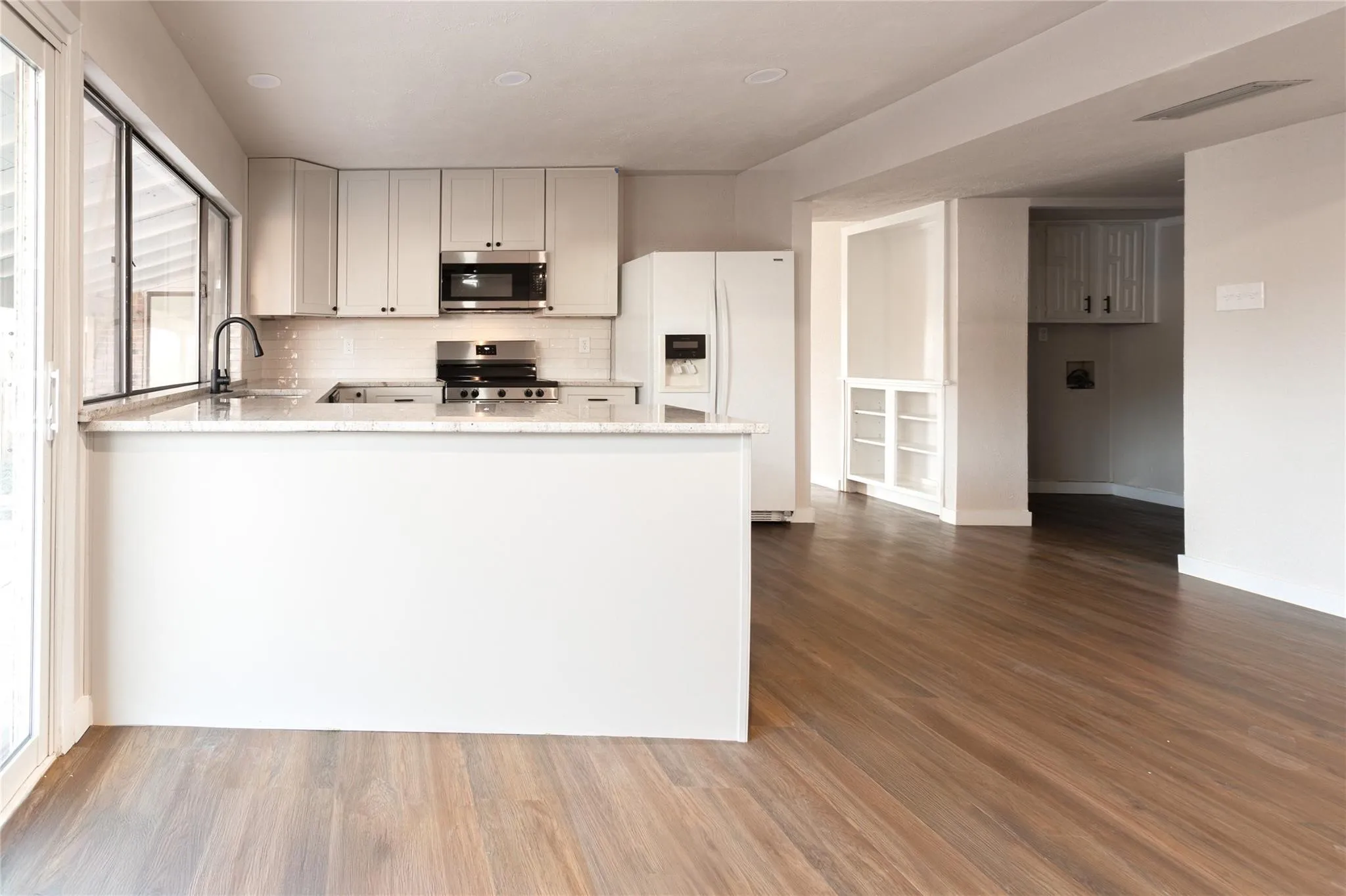 Kitchen with wood-finish flooring, recessed lighting, light-toned cabinetry, stainless steel appliances, and a full-height tile backsplash
