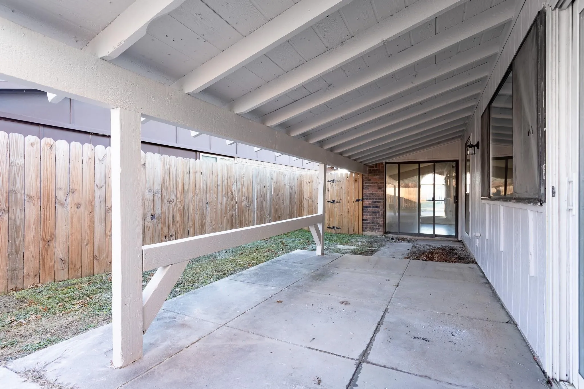 Covered patio with concrete flooring, exposed white wood beams, and direct access to interior via glass sliding doors