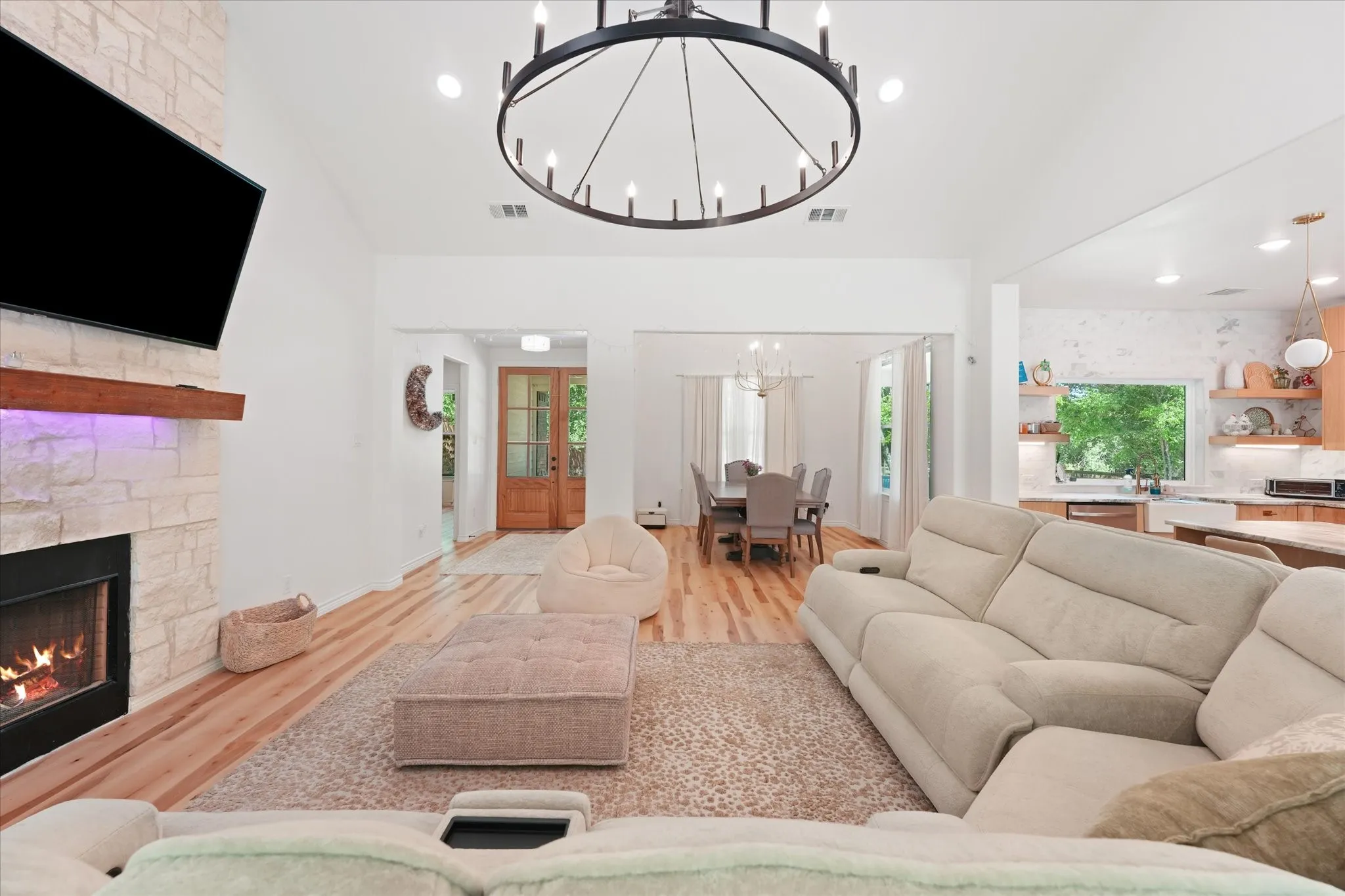 Vaulted ceiling with an oversized chandelier, stone-faced fireplace with a wood mantle, wood-finish flooring, and recessed lighting
