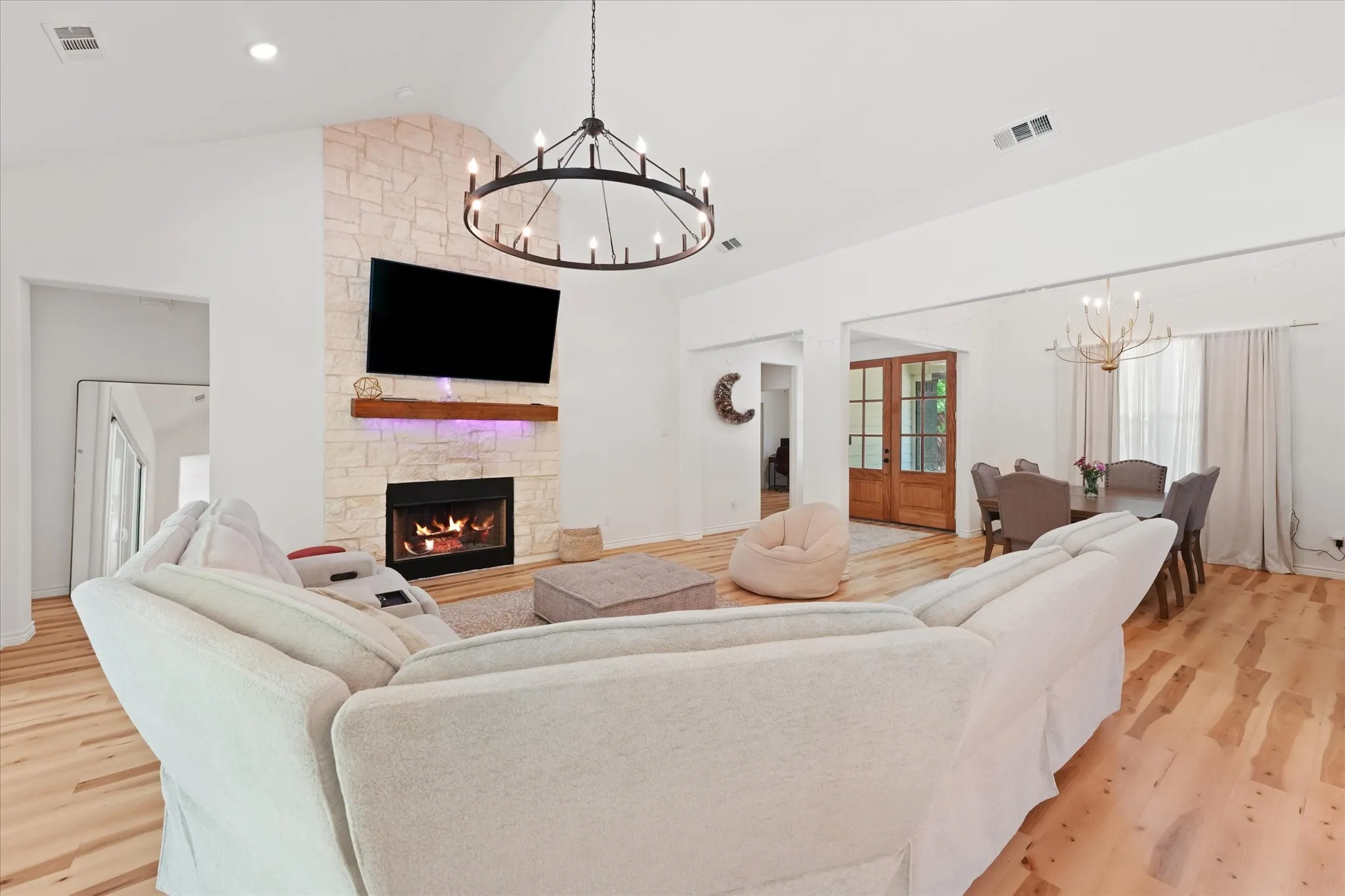 Vaulted ceiling, stone-clad fireplace, wood-finish flooring, recessed lighting, and a circular chandelier