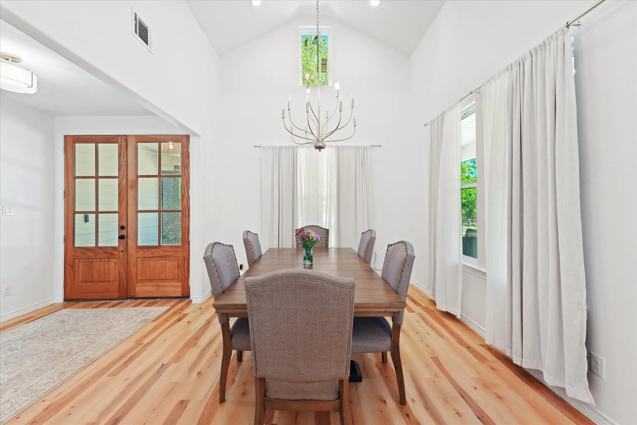 Vaulted ceiling with a skylight, wood-finish flooring, double glass-paned entry doors, and a chandelier
