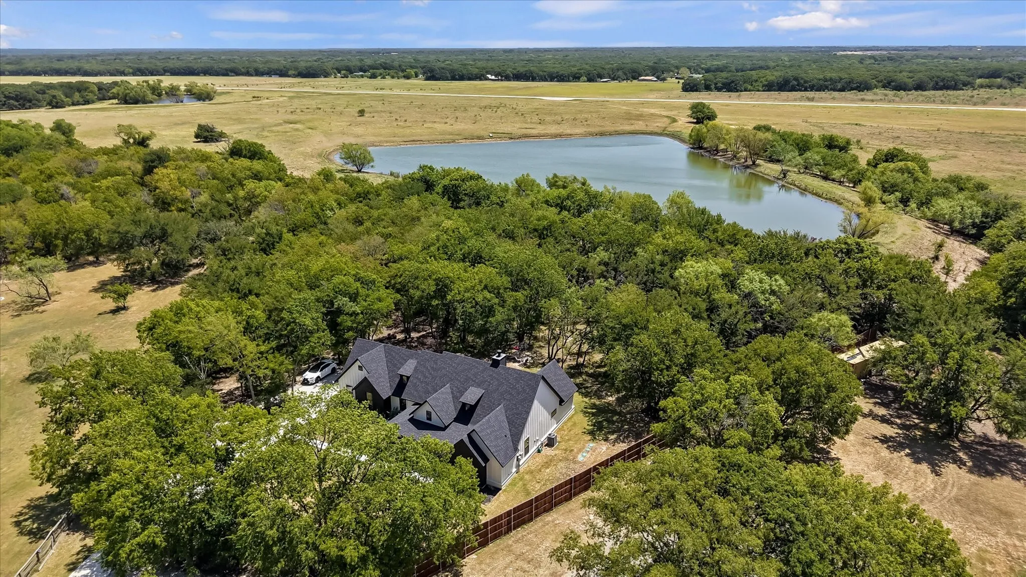 Expansive acreage featuring a private pond, mature trees, and a residential structure with a dark shingle roof