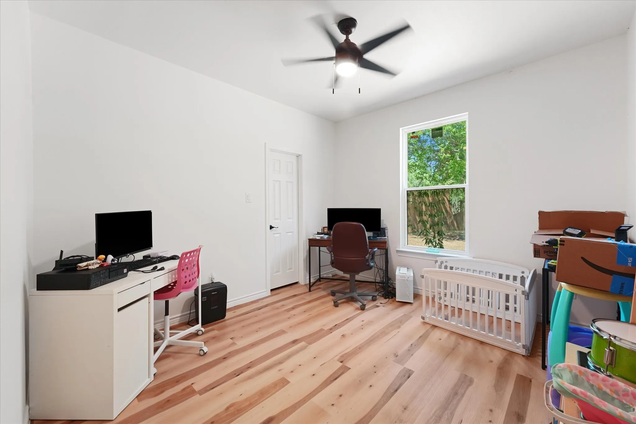 Room featuring wood-finish flooring, a ceiling fan with integrated lighting, a paneled door, and a prominent window