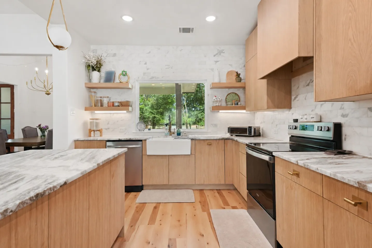 Wood-finish cabinetry, light wood-finish flooring, white brick-pattern backsplash, white farmhouse sink, and a large center island with a stone countertop