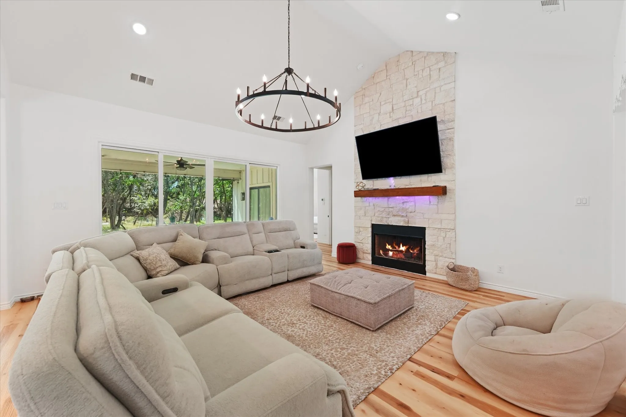 Vaulted ceiling with an open-concept layout, stone-clad fireplace, wood mantel, wood-finish flooring, and sliding glass doors