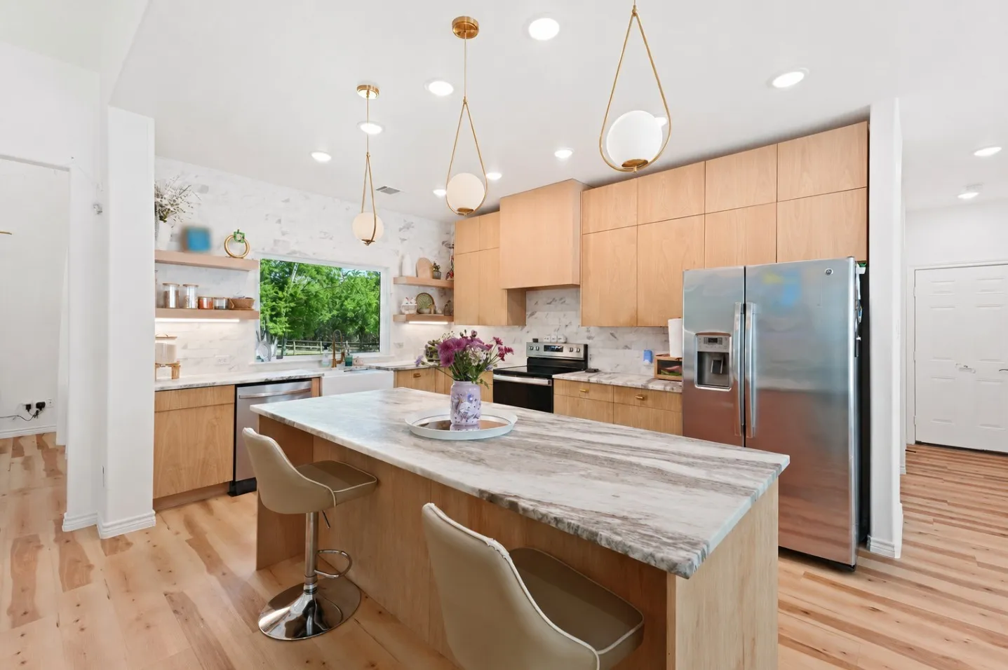 Kitchen featuring light wood-finish cabinetry, stainless steel appliances, a large center island with a stone countertop, and open shelving