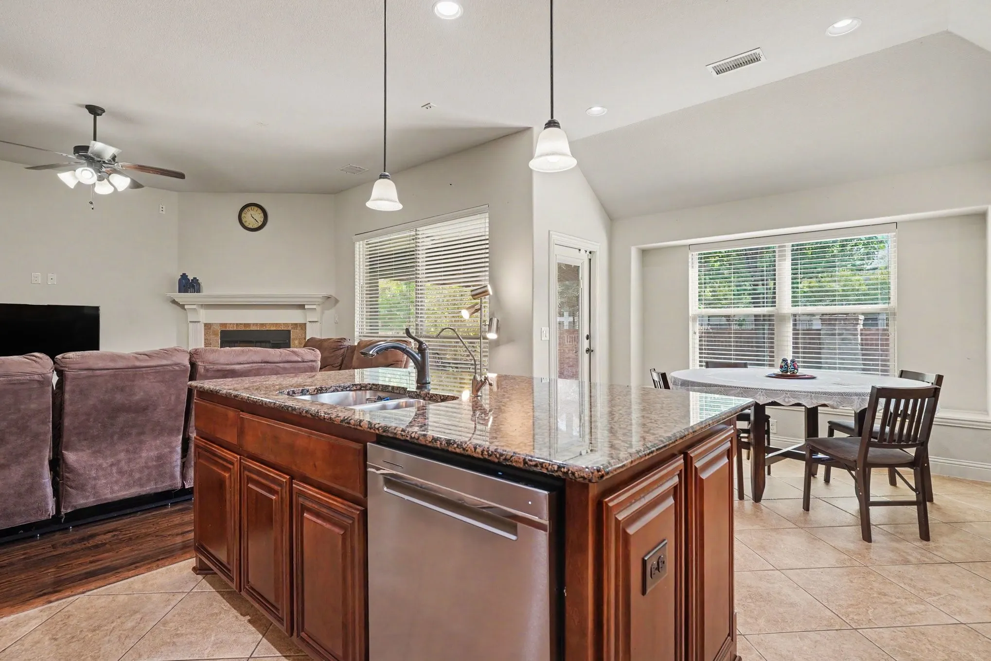 Kitchen island with granite countertop, integrated stainless steel dishwasher, and pendant lighting