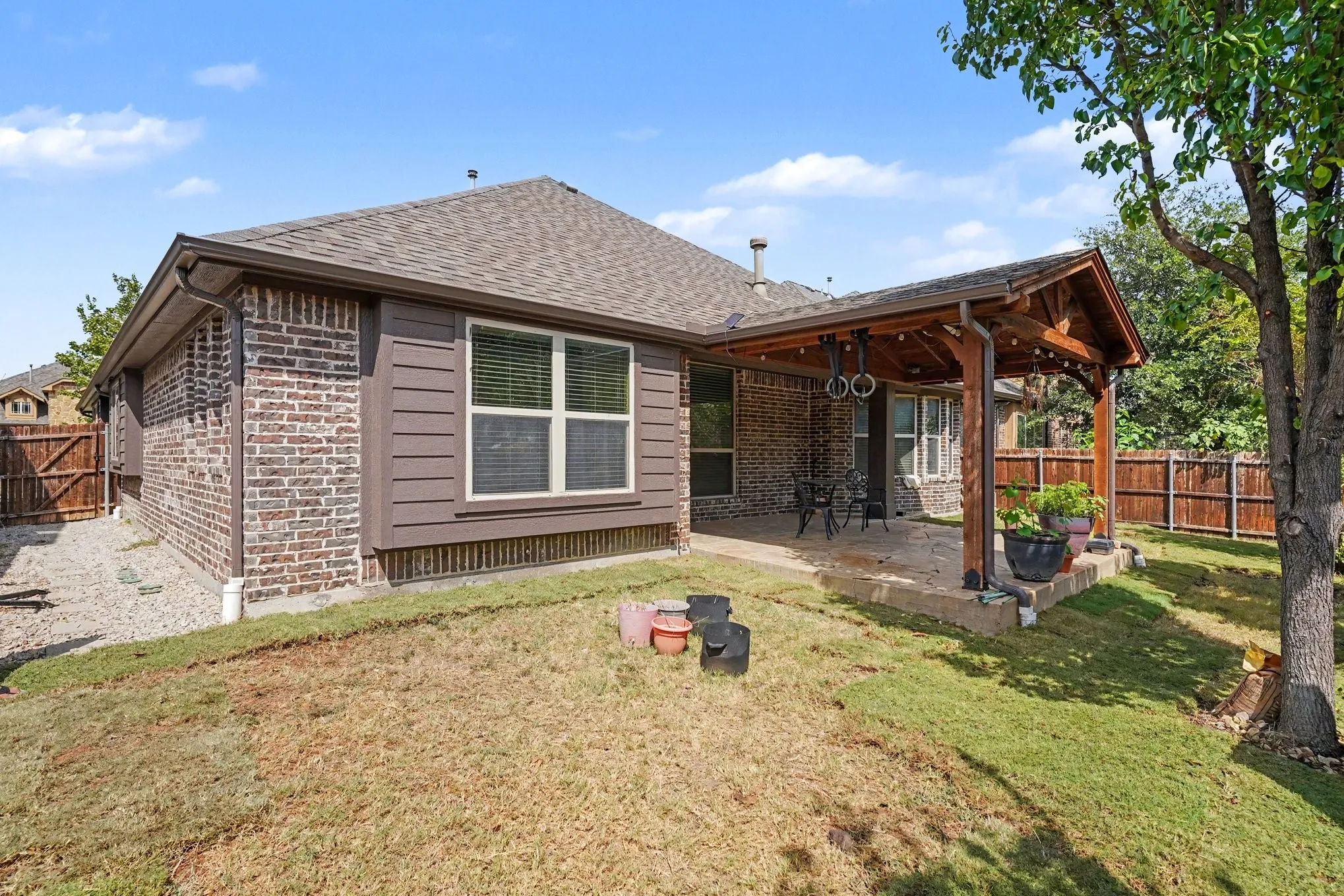 Brick exterior with horizontal siding accents, covered patio with wood beam structure, fenced perimeter, and a sloped lawn