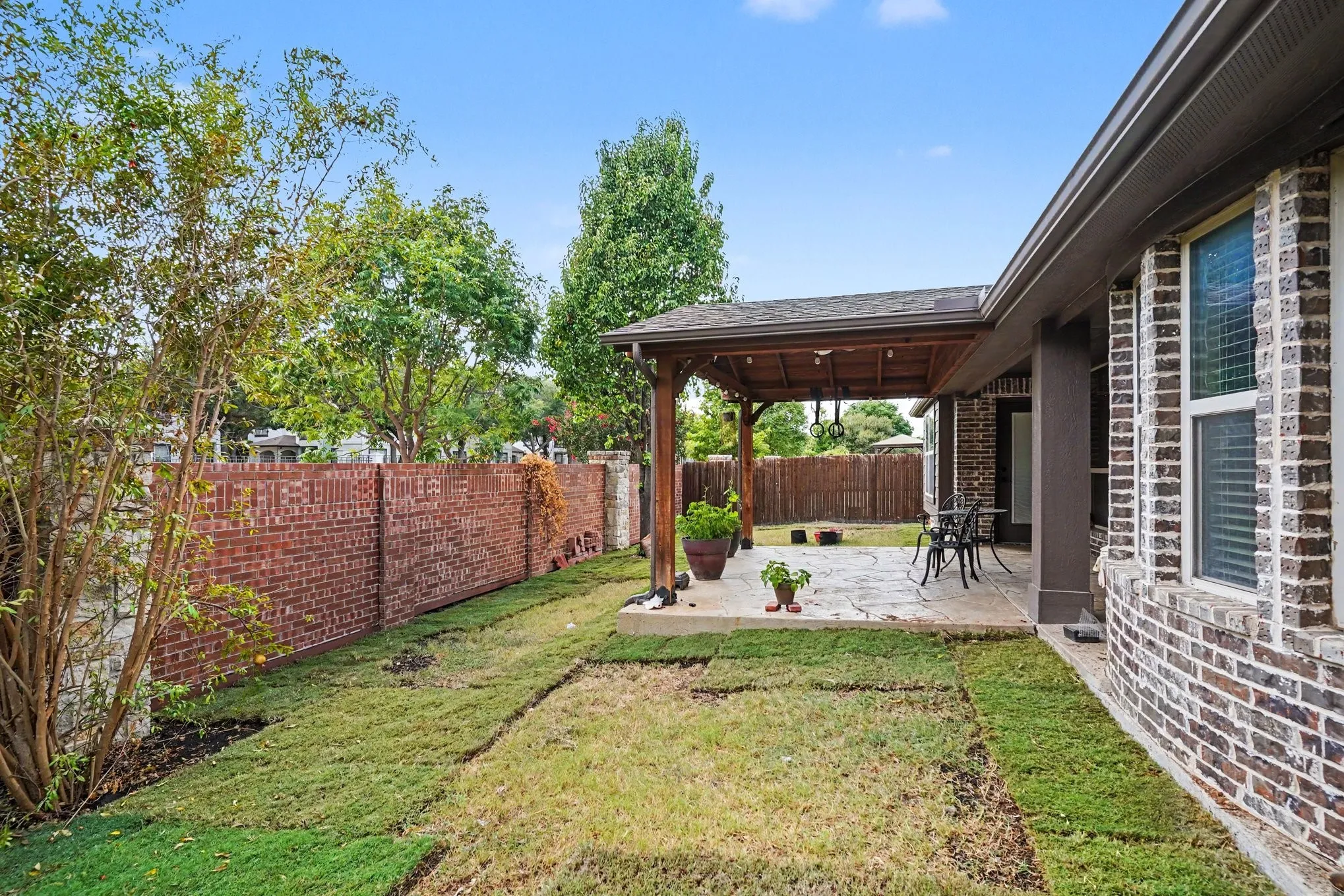 Covered patio with a wood pergola, brick exterior siding, and a stone patio surface