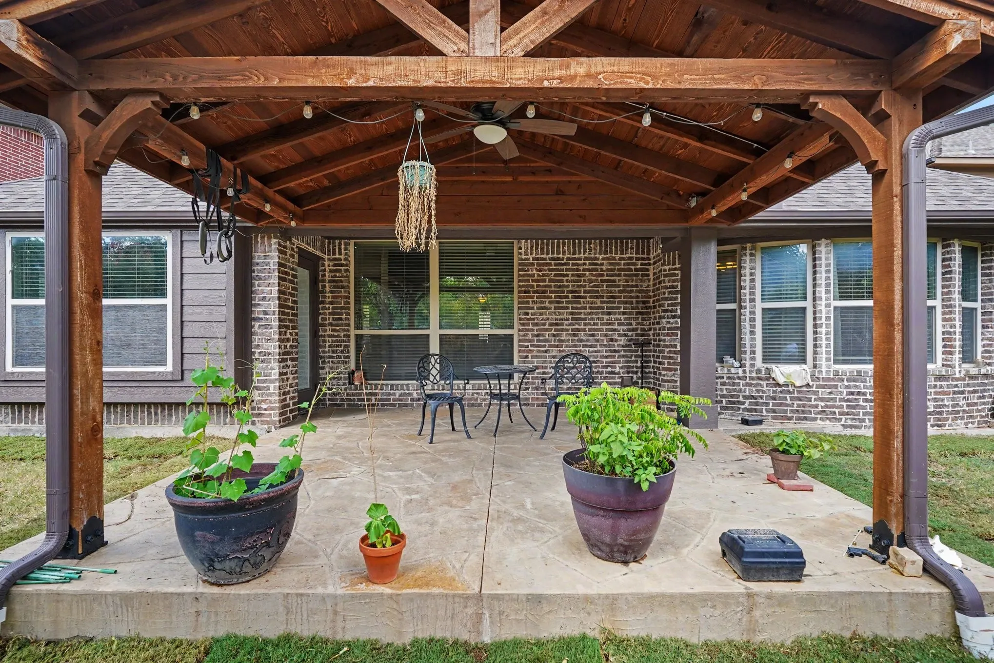 Expansive covered patio featuring a wood-beamed ceiling, stamped concrete flooring, brick exterior, and multiple windows