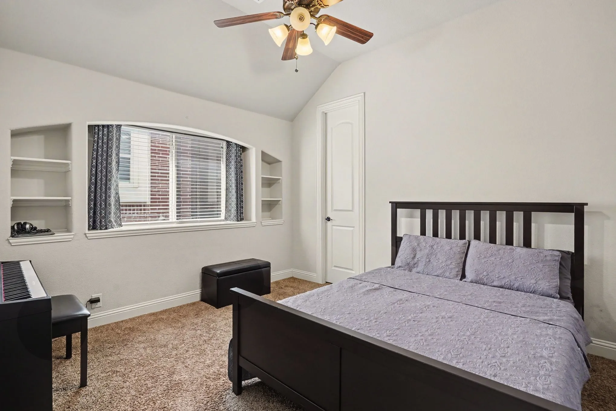 Vaulted ceiling with a ceiling fan light fixture, arched window with integrated blinds, and built-in shelving