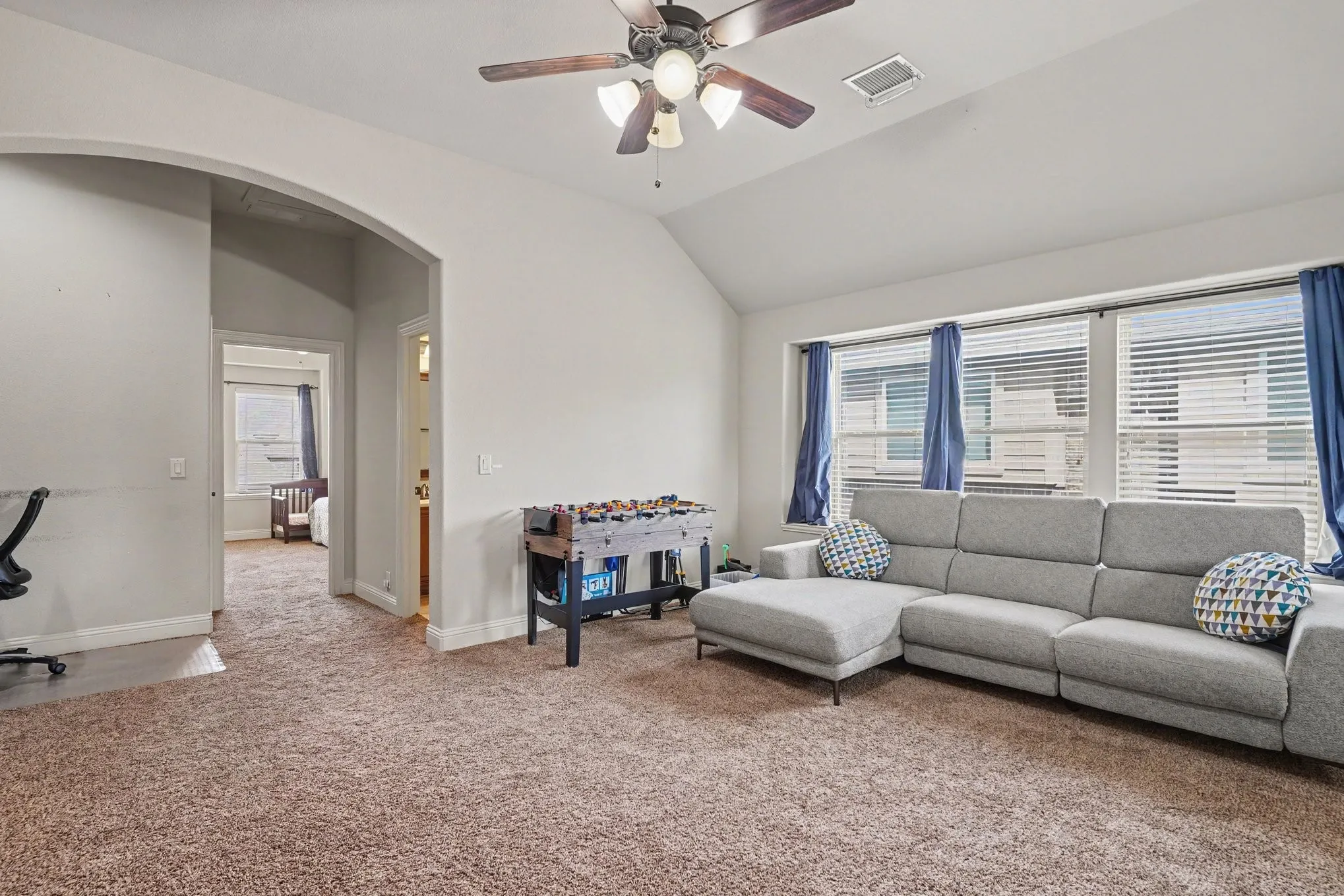 Vaulted ceiling with a ceiling fan, arched doorway, and large windows with blinds