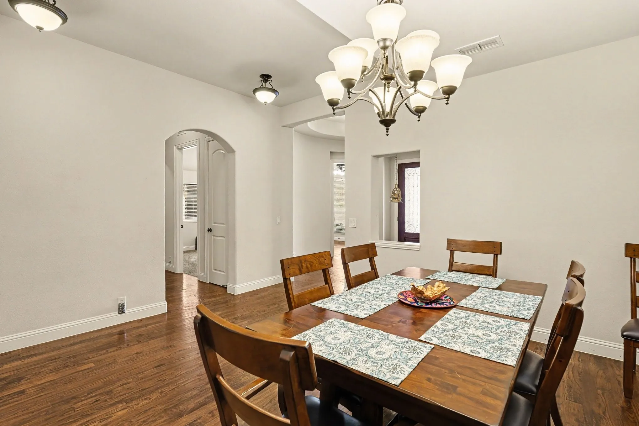 Hardwood-finish flooring, recessed ceiling with a central chandelier, arched doorway, and built-in wall niche