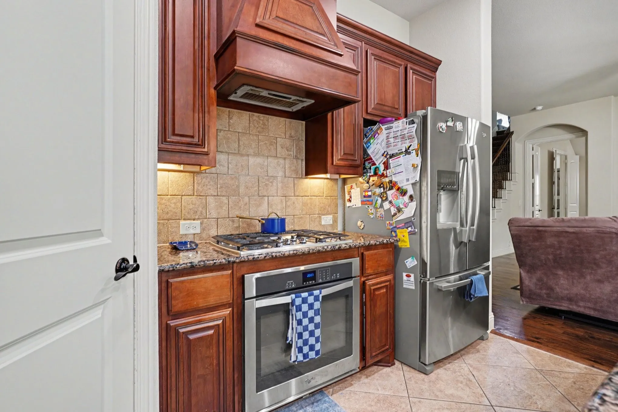 Rich wood cabinetry with crown molding, granite countertops, tile backsplash, and stainless steel appliances