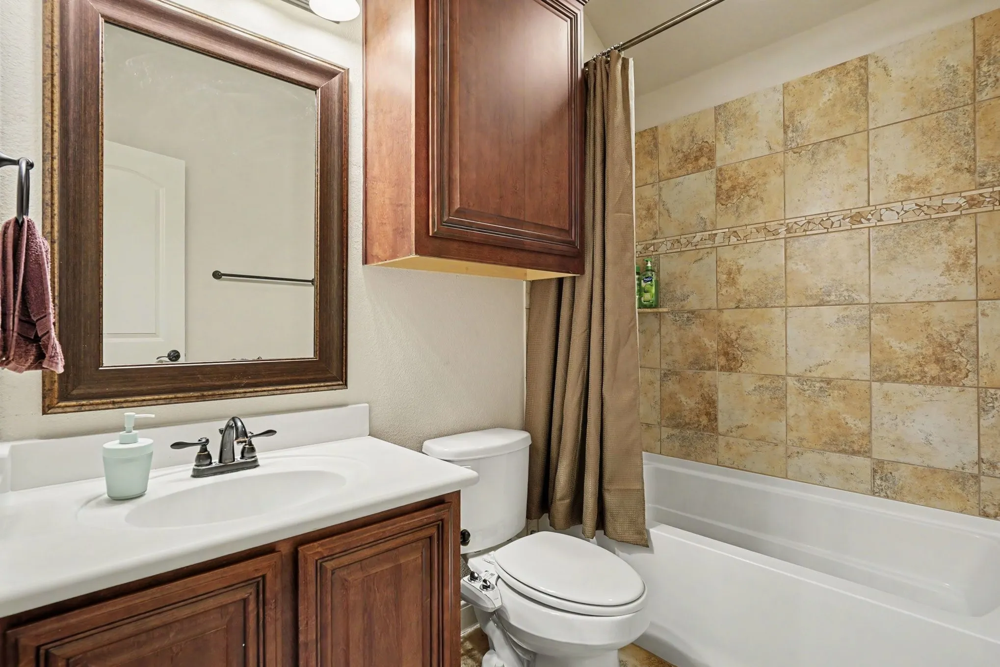 Bathroom featuring a white vanity with an integrated sink, dark wood cabinetry, a framed mirror, and a tiled shower-bath combination