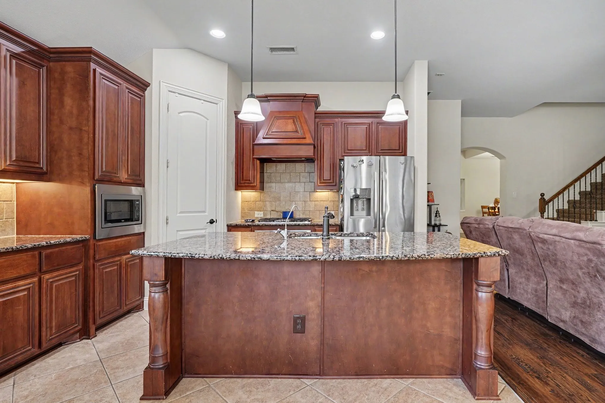 Kitchen featuring wood cabinetry, an integrated microwave, stainless steel refrigerator, and a kitchen island with pendant lighting