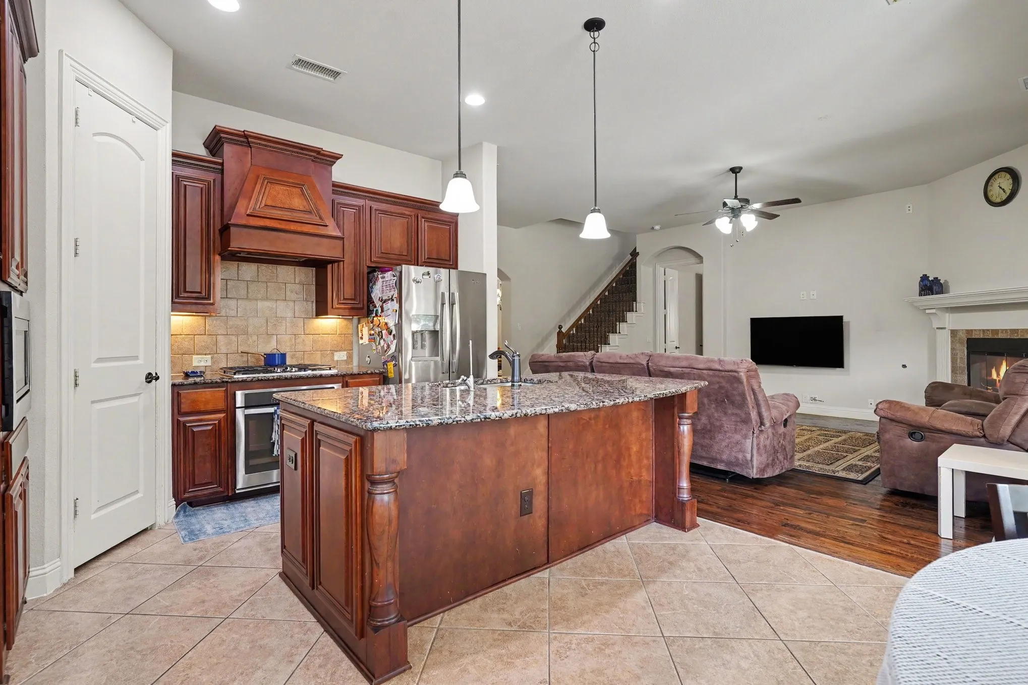 Kitchen island with stone countertop, tile flooring, stainless steel appliances, wood cabinetry, and a stone fireplace