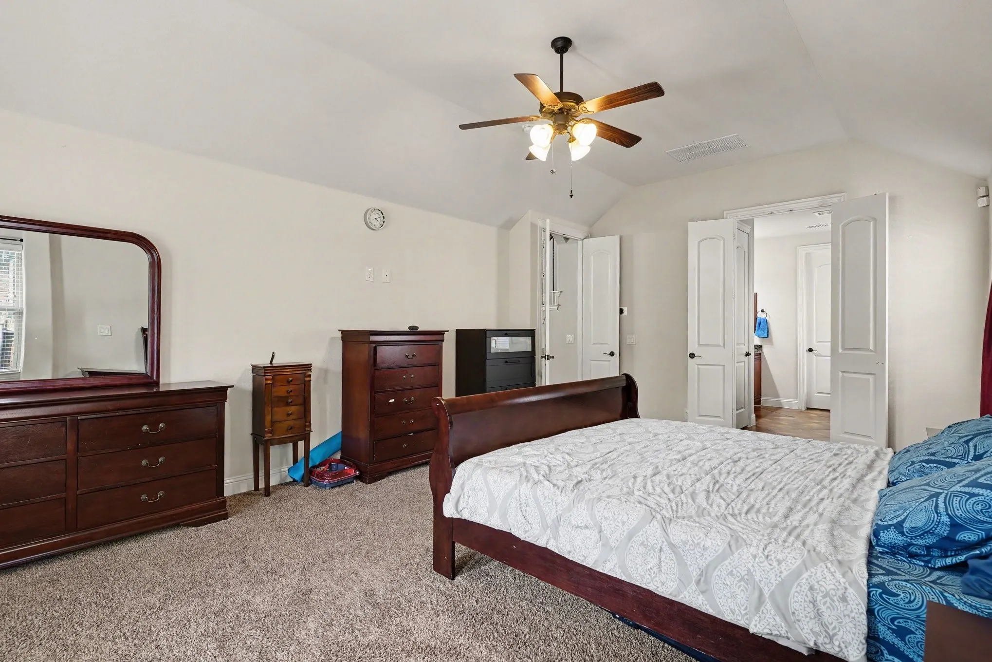 Carpeted room with a vaulted ceiling, a ceiling fan with integrated lighting, and multiple white paneled doors
