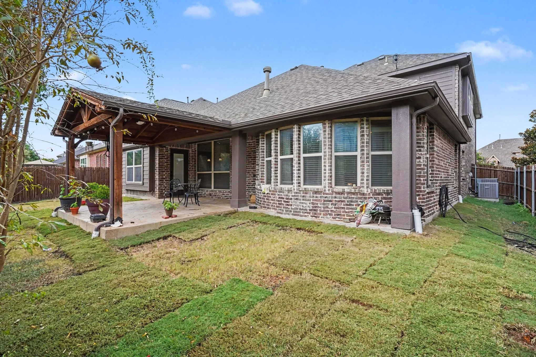 Brick exterior with multiple windows, covered patio with wood beam accents, and a shingle roof
