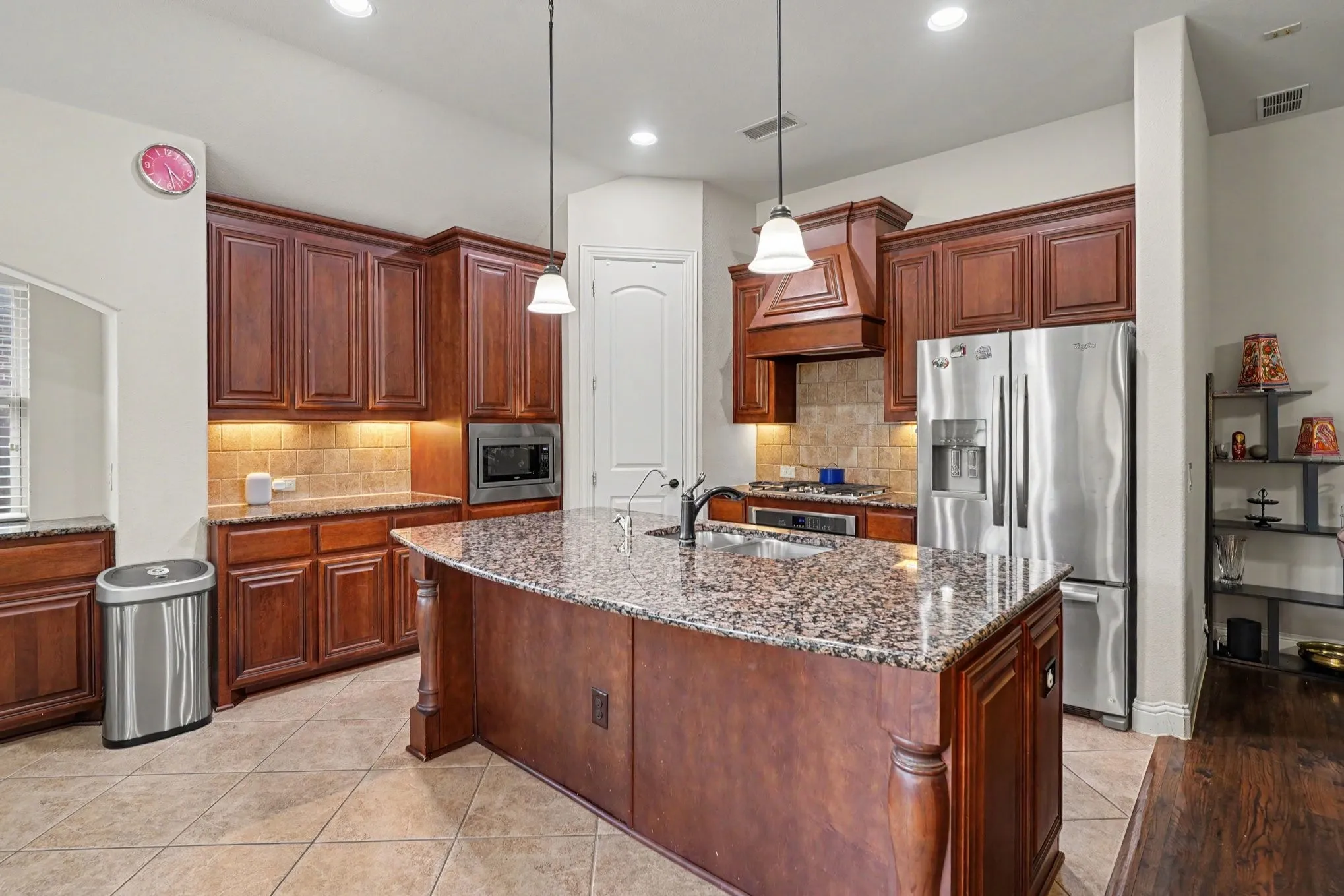 Kitchen featuring an island with stone countertops, wood cabinetry, stainless steel appliances, and tile flooring