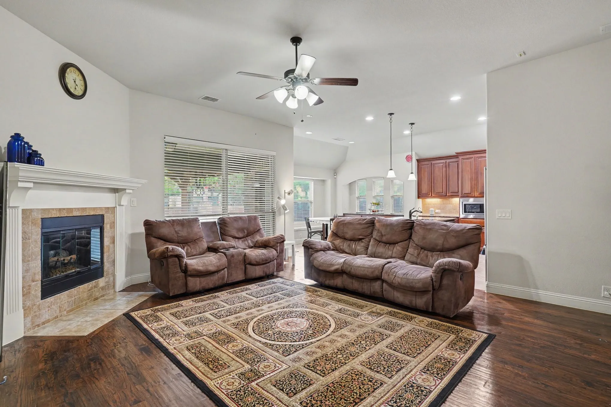 Living room featuring a fireplace with a tile surround, dark wood-finish flooring, and a ceiling fan