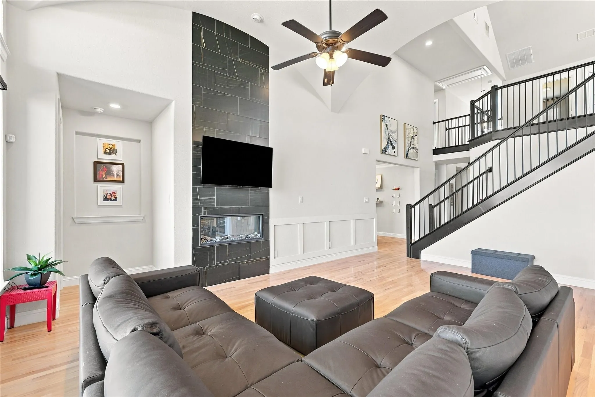 Vaulted ceilings, wood-finish flooring, a contemporary fireplace with a dark tile surround, a built-in recessed niche, and an open staircase with dark railings