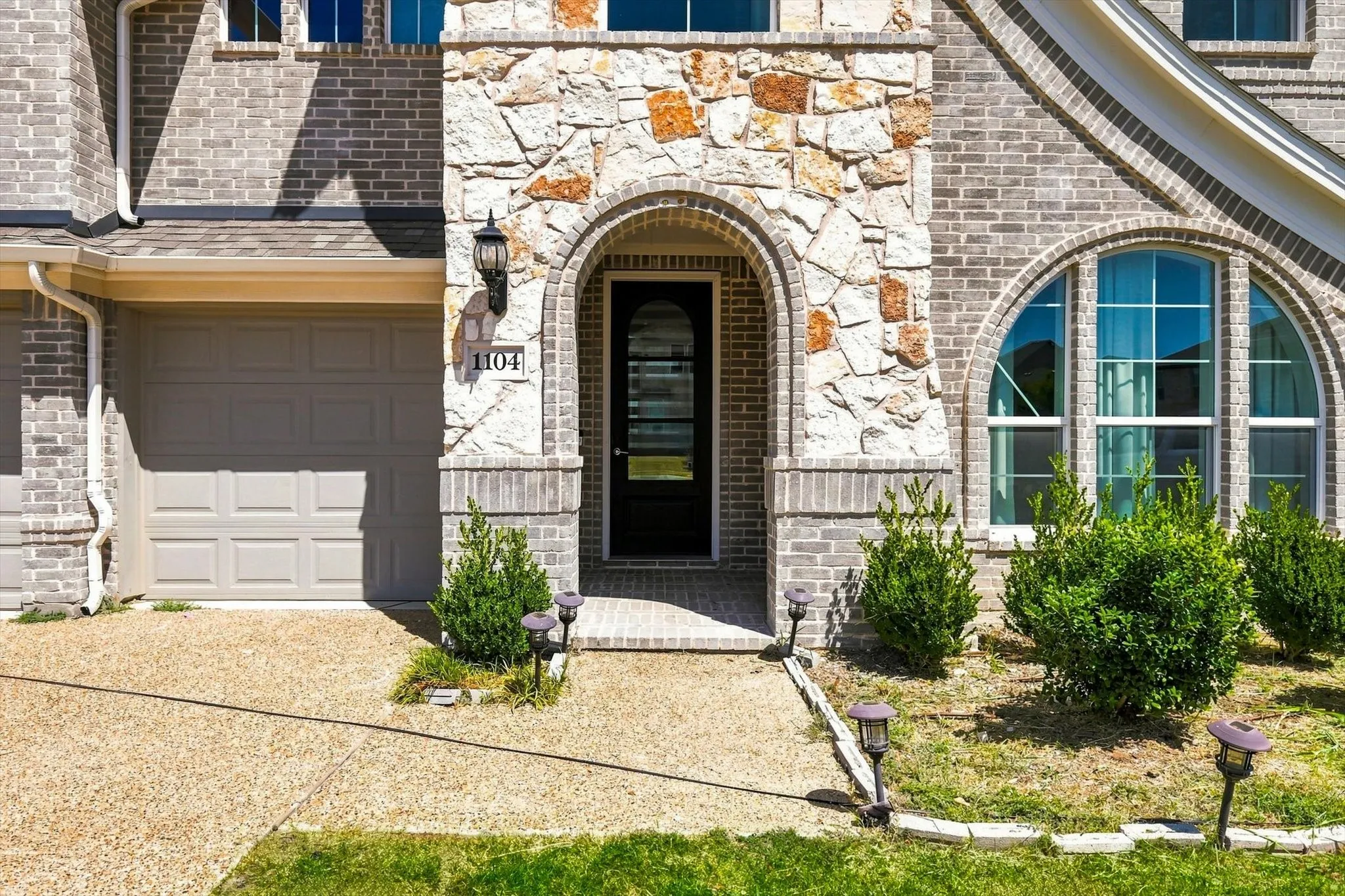 Brick and stone veneer exterior with an arched entry, a panel garage door, an arched window, and a concrete driveway