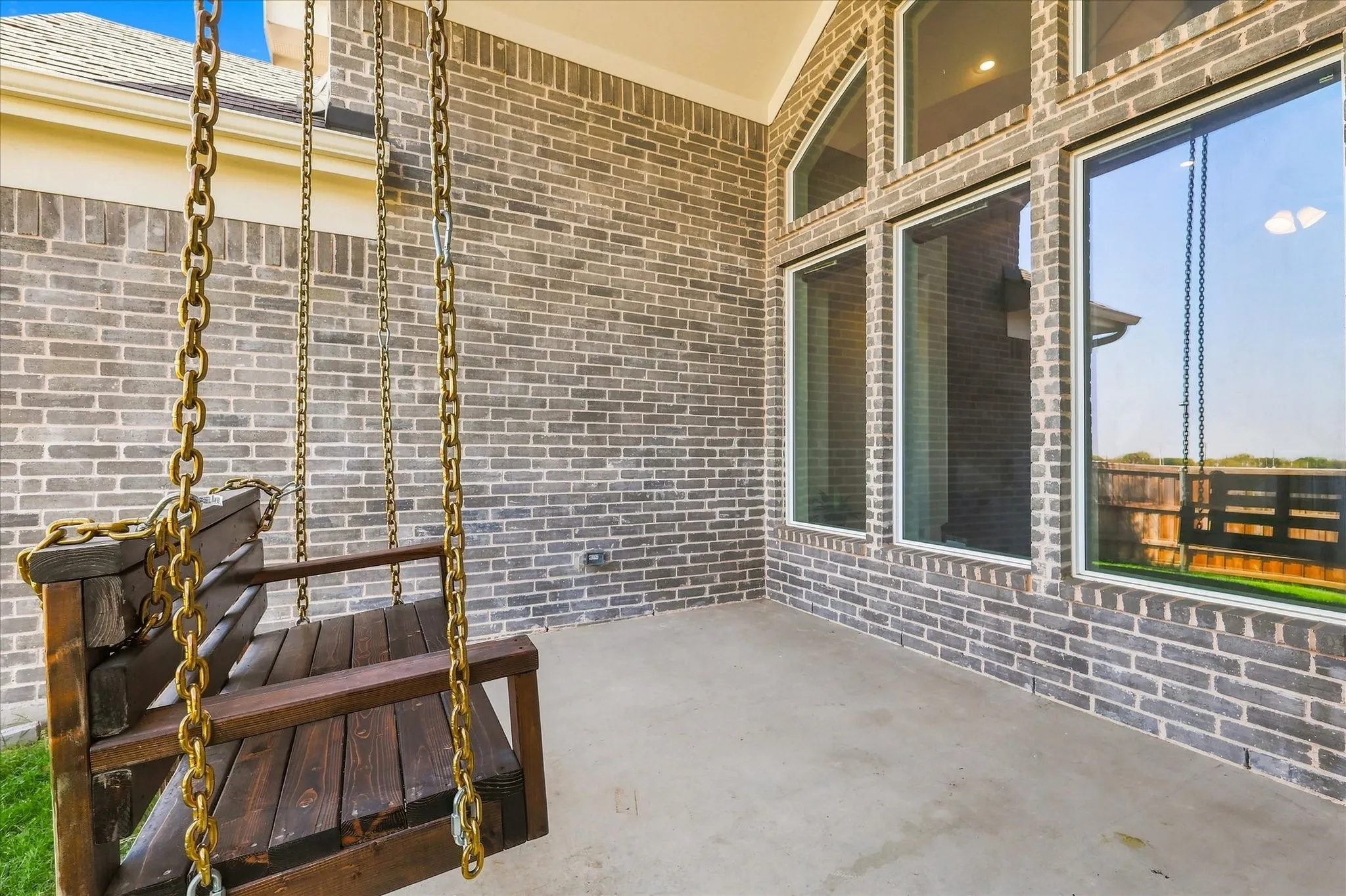 Covered patio with brick siding, multiple large windows, and a wood porch swing with chain suspension
