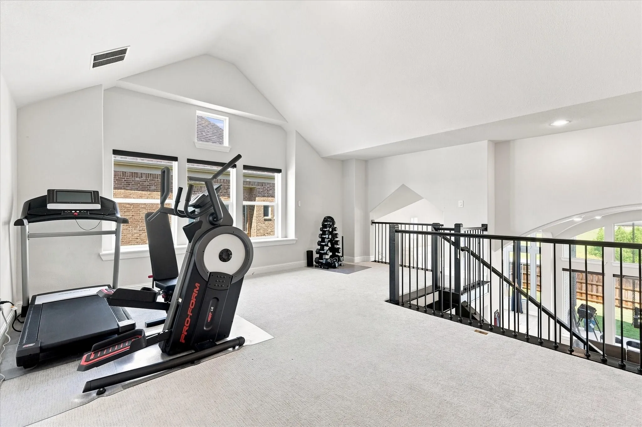 Vaulted ceiling with recessed lighting, multiple windows, carpet flooring, and black metal railing