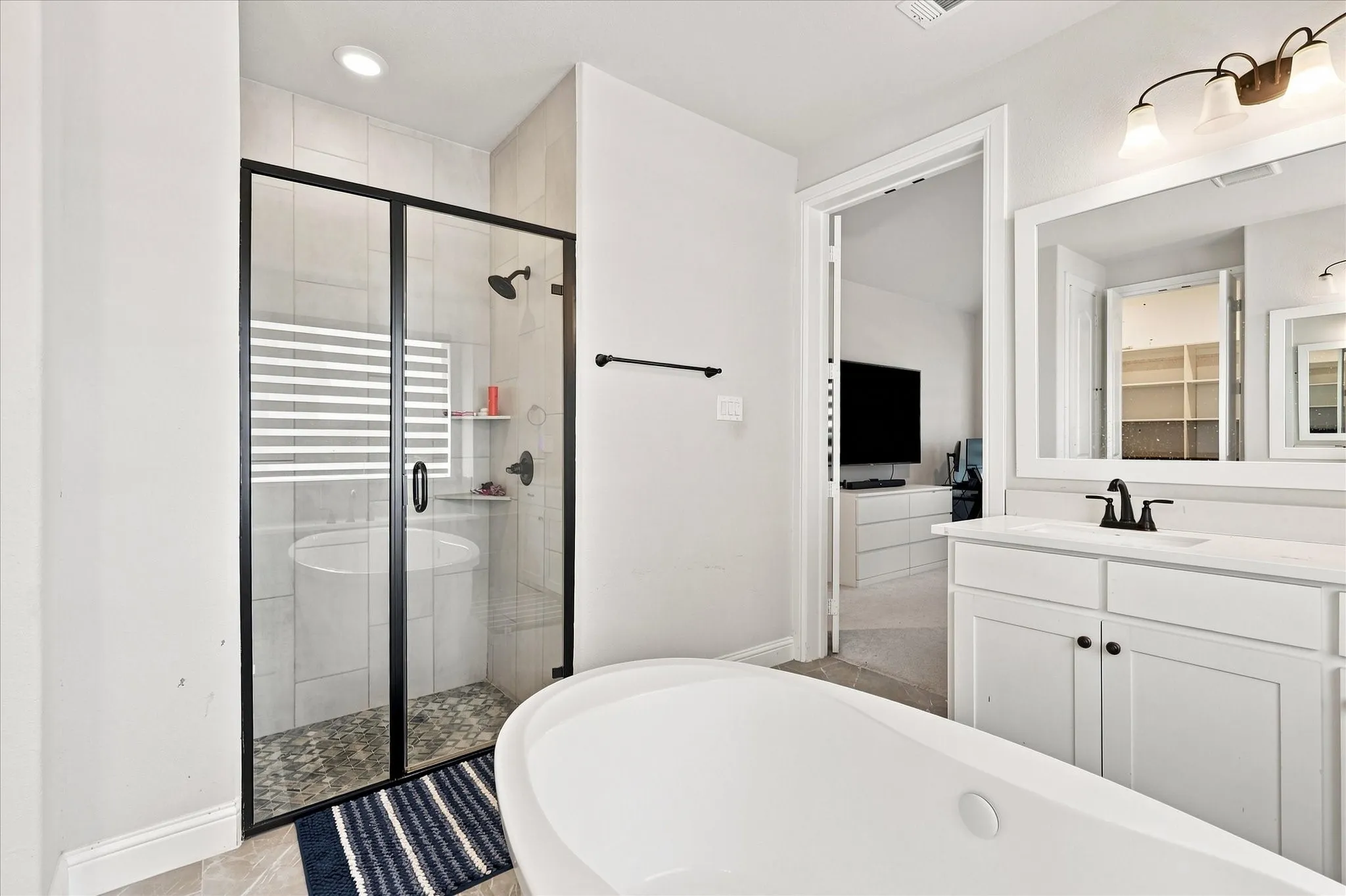 Freestanding soaking tub, walk-in shower with matte black frame, single vanity with white cabinetry, and a large wall-mounted mirror