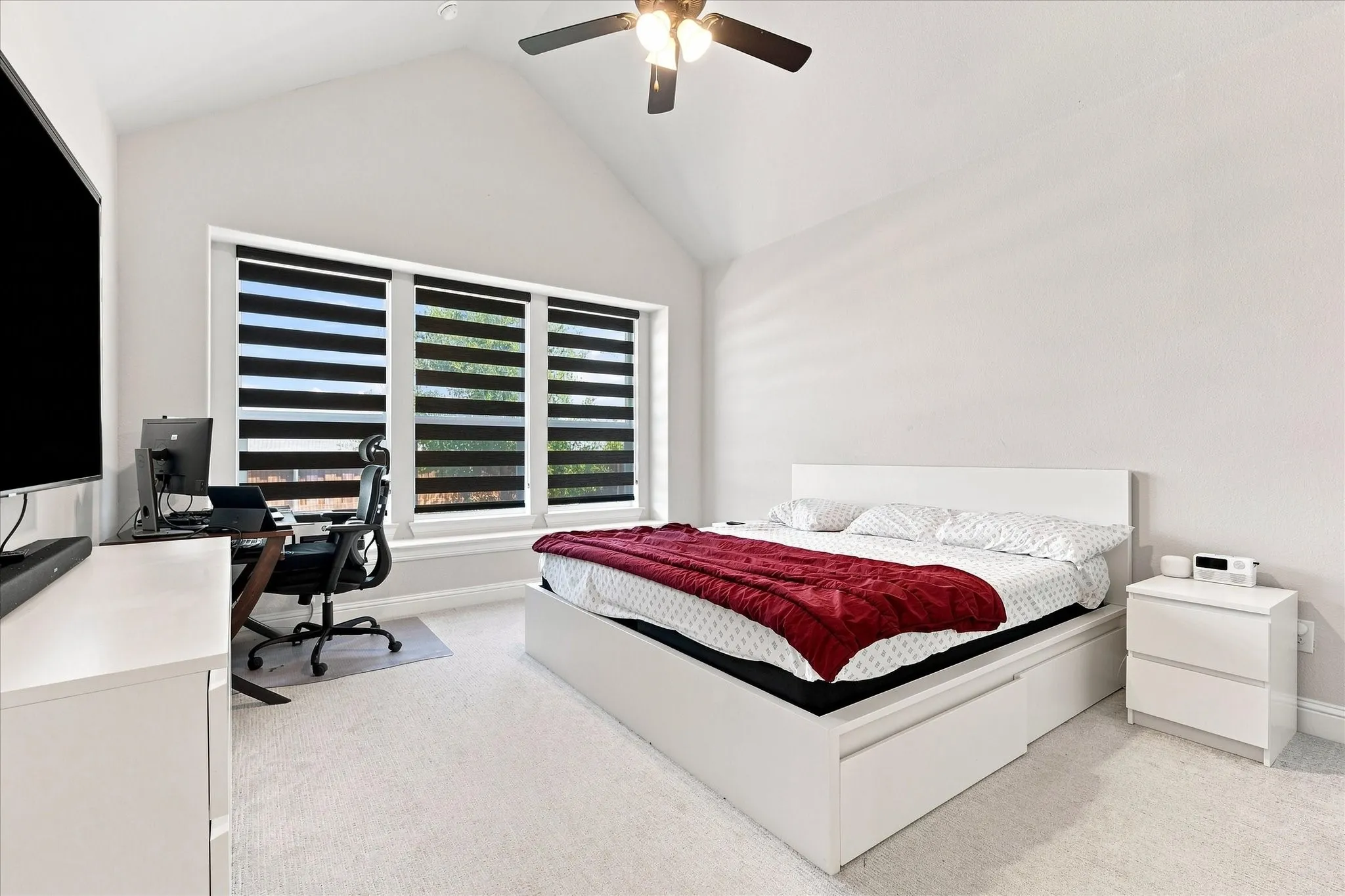 High vaulted ceiling with a ceiling fan, large windows with horizontal blinds, and light-colored carpeting