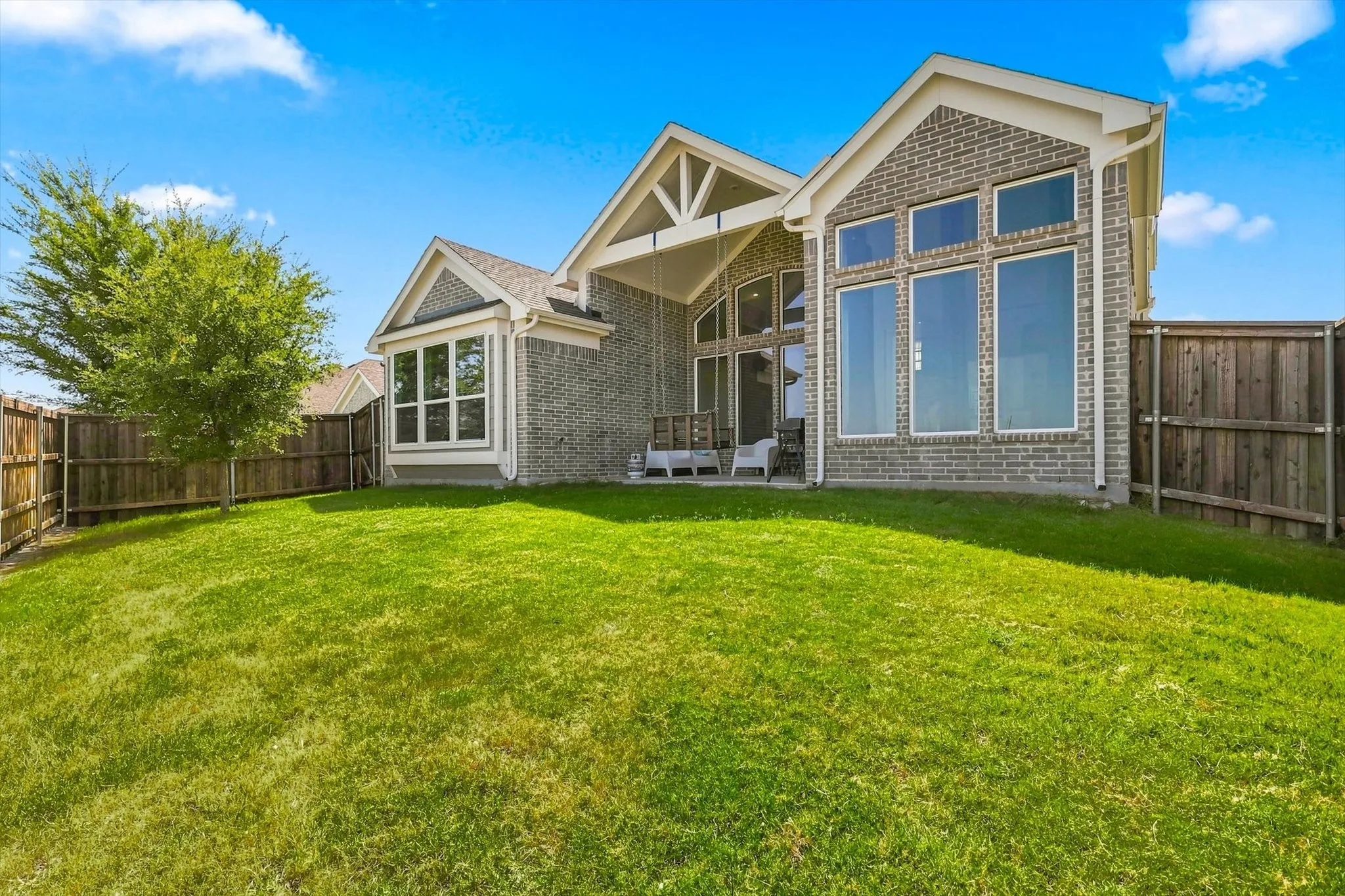 Expansive grassy yard with wood fencing, a shaded covered patio, and large windows